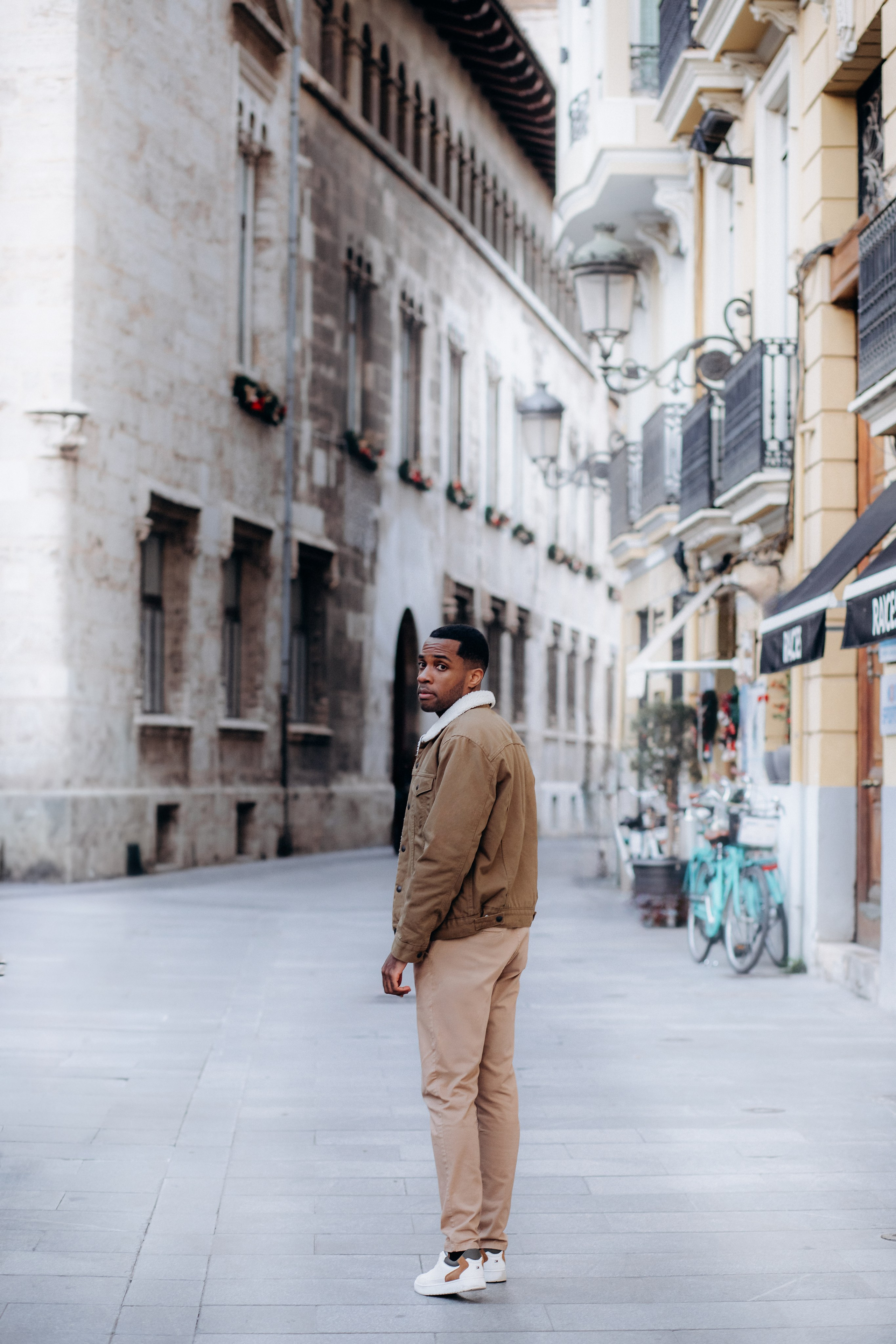 Мужская портретная фотосессия в Валенсии, Испания, со стильным мужчиной, идущим по исторической улице старого города с каменной архитектурой, мягким естественным светом и кинематографичной городской атмосферой, создающей расслабленное, но уверенное настроение — идеально для мужской портретной фотографии, lifestyle-фотосессий для мужчин, городских портретов, сессий для персонального бренда и профессиональных мужских фотосессий в Валенсии и по всей Испании.