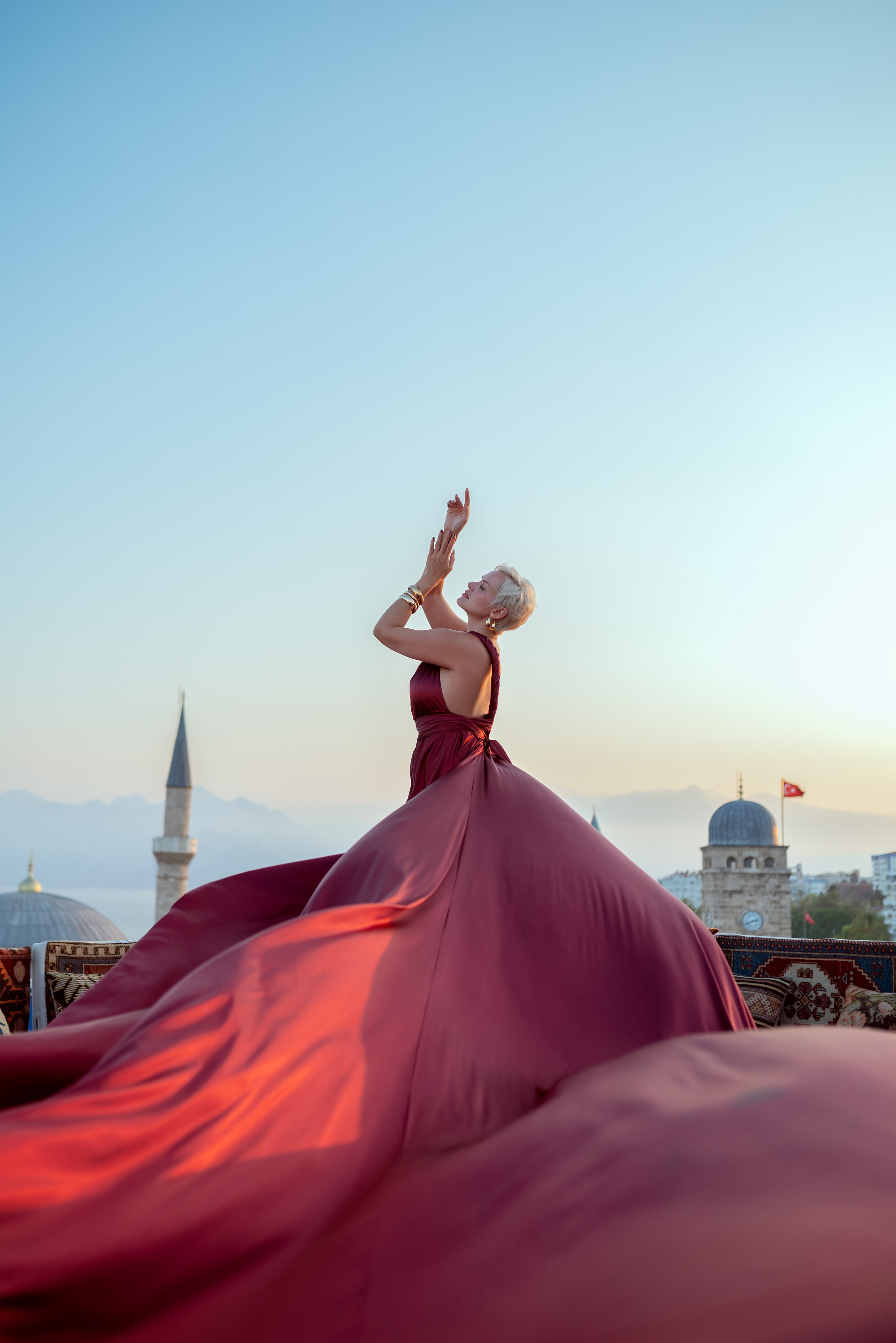 Фото девушки в платье со шлейфом на крыше среди турецких ковров с видом на море в Турции