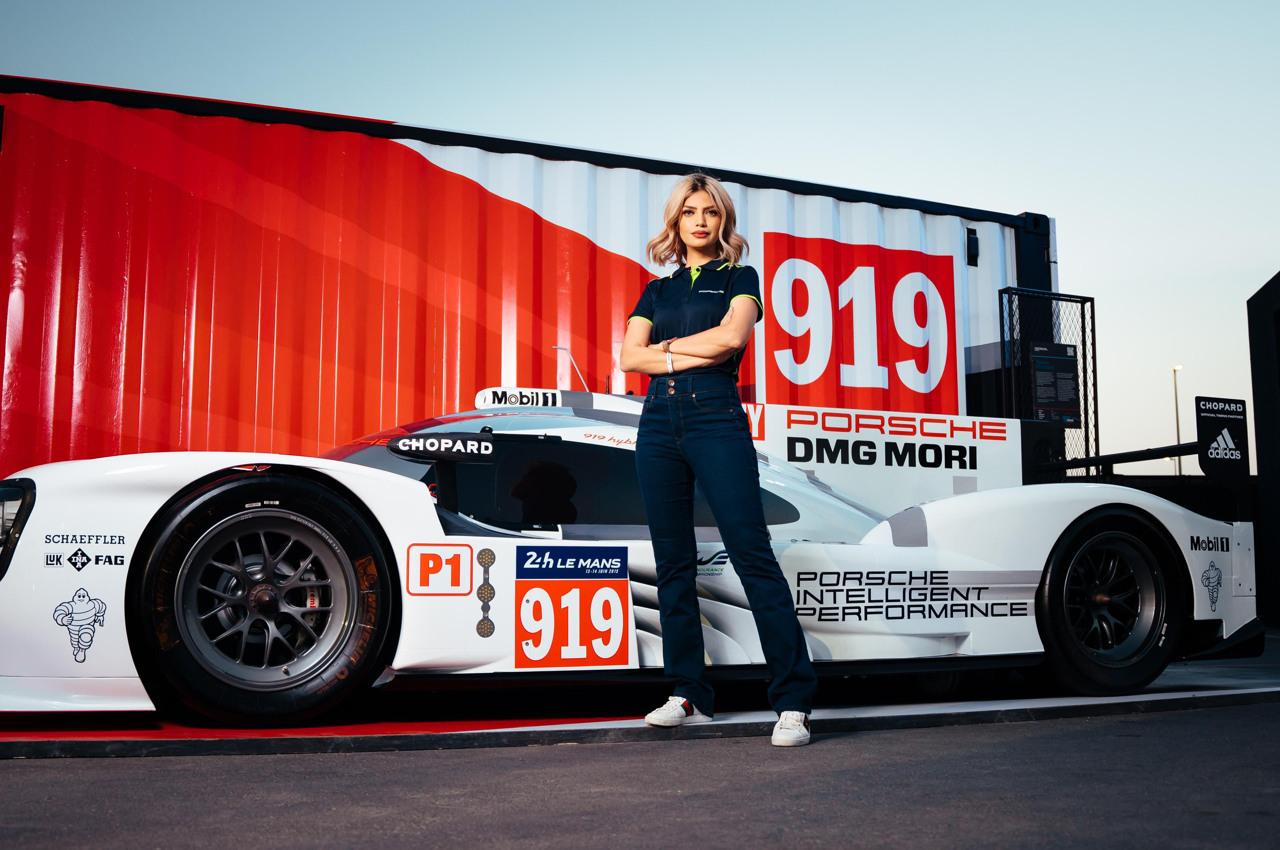 A girl stands next to a white sports car with the number 919