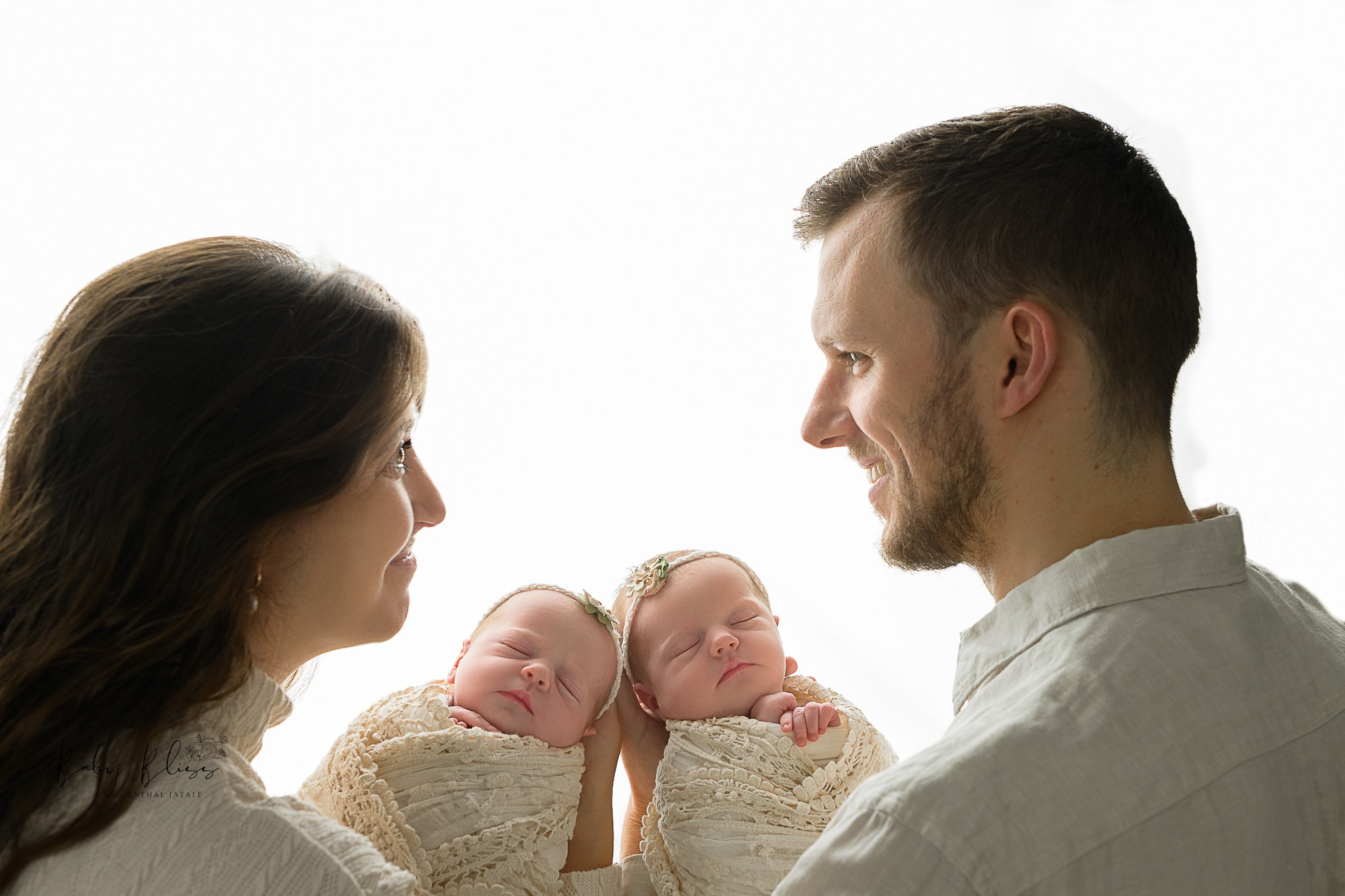 twins newborn baby girls are held by their parents in whitish colour outfits showing soft and neutral aesthetic  tones.