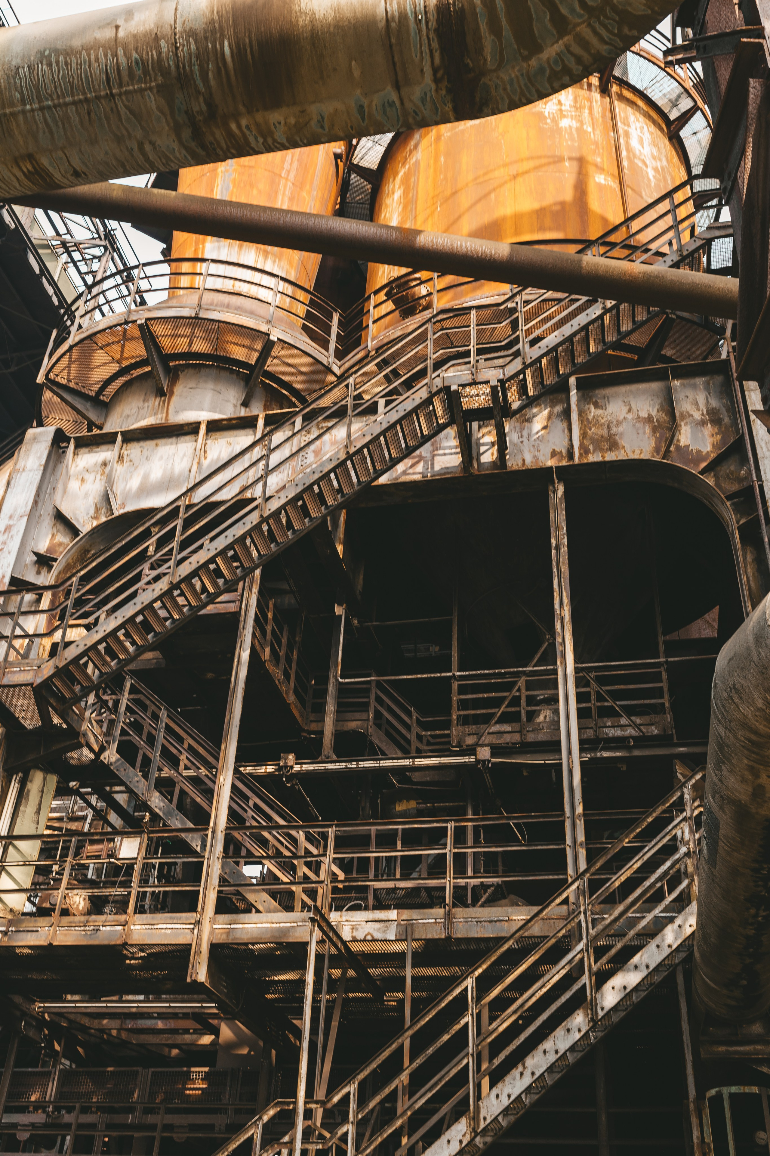 Узкая ржавая лестница, ведущая на верхний уровень промышленного помещения.