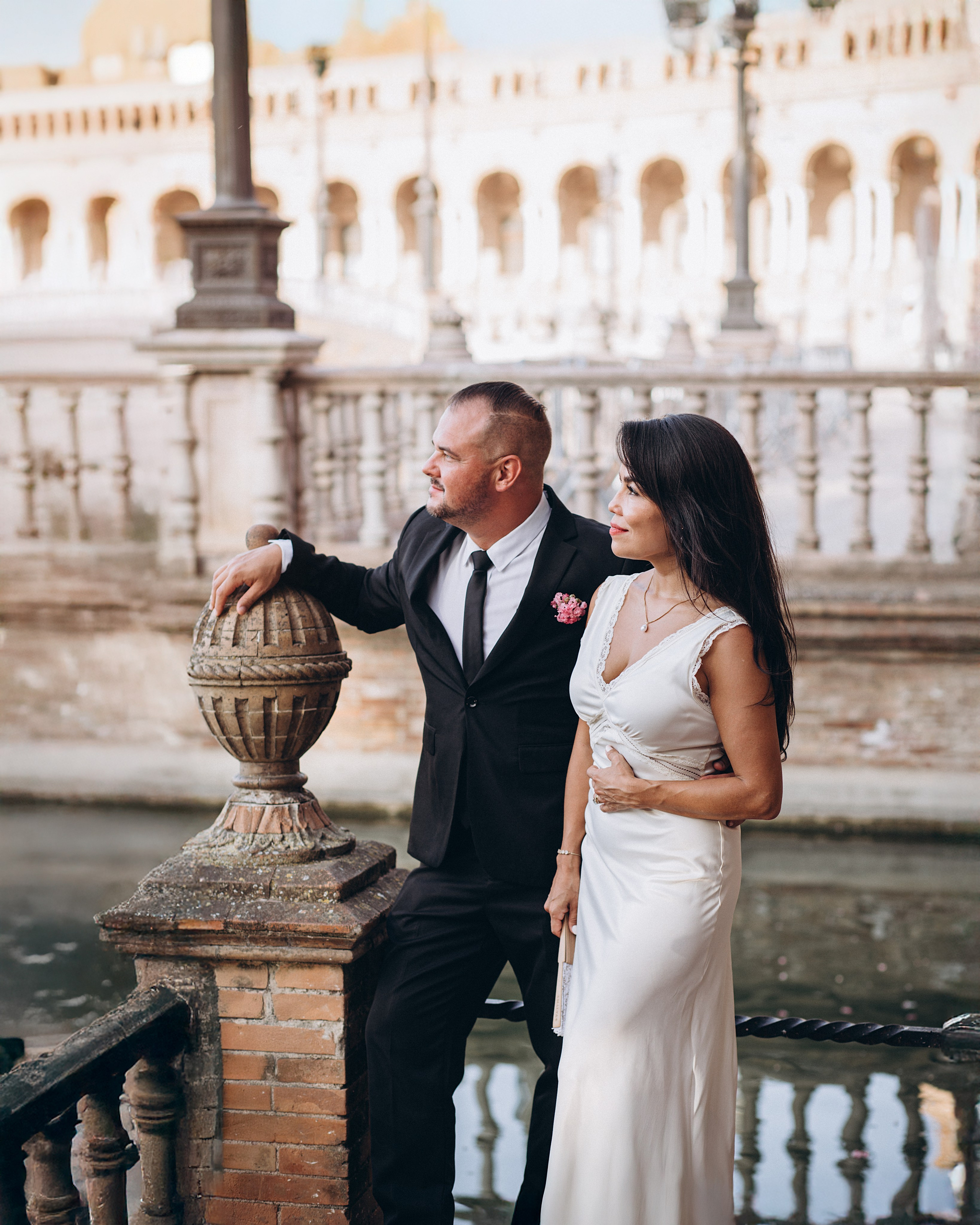 Newlyweds standing by the ornate balustrade at Plaza de España, overlooking the historic square in Sevilla. Romantic civil wedding portrait blending classic Spanish architecture with natural emotion.