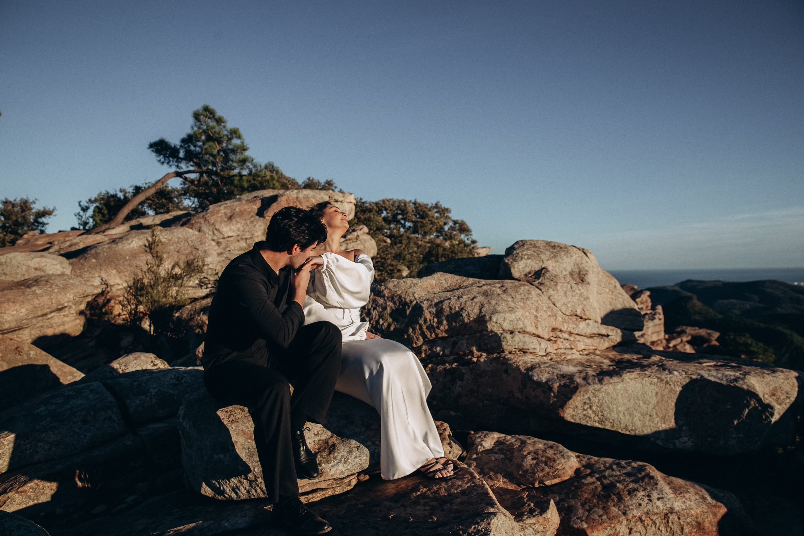Newlyweds sitting together on rocky cliffs overlooking the mountains during an intimate destination wedding in Barcelona, Spain. This romantic elopement moment highlights the beauty of a private outdoor ceremony.