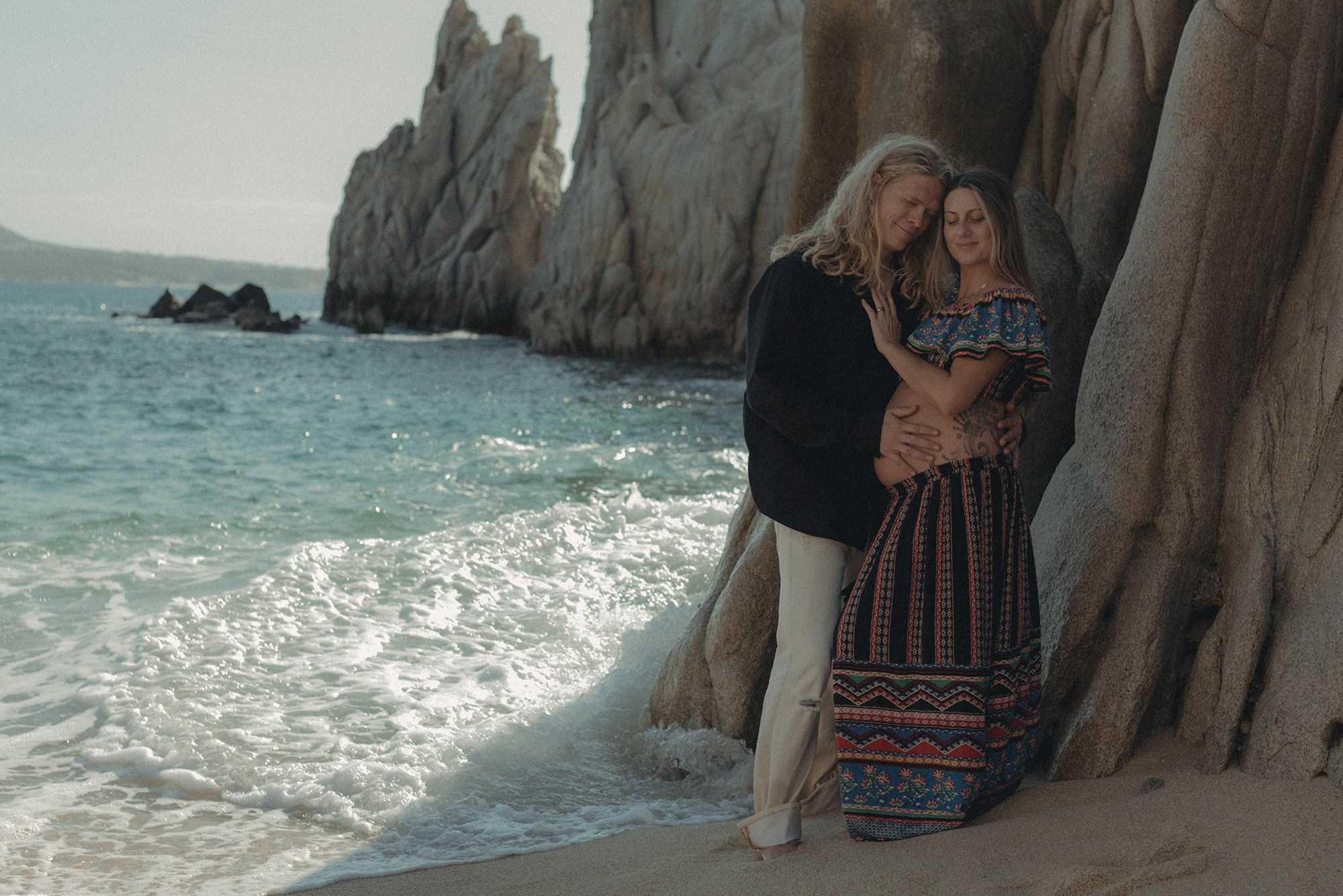 Cinematic maternity portraits in Cabo San Lucas – mother-to-be at Playa del Amor with dramatic rocks and beach scenery, edited with cinematic tones, professional maternity and family photographer