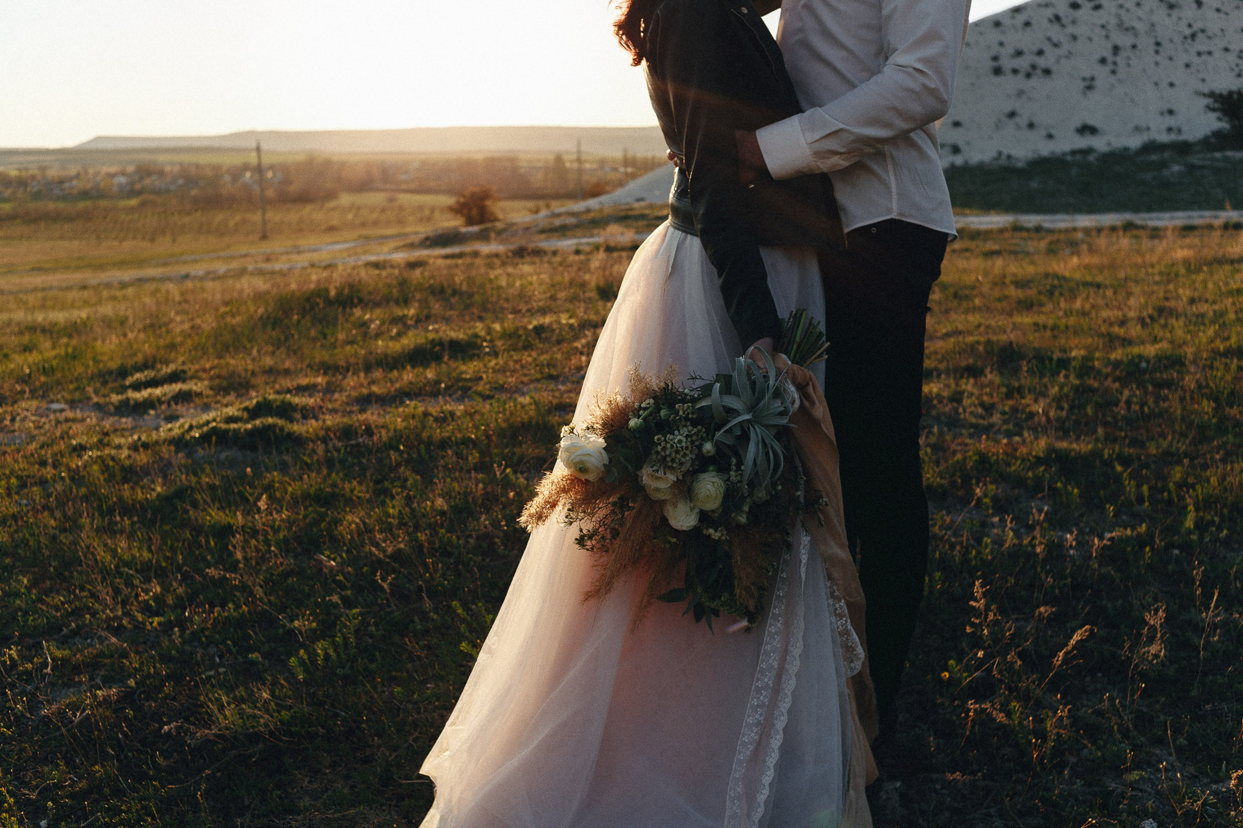 Bride standing with bouquet at sunset in open field