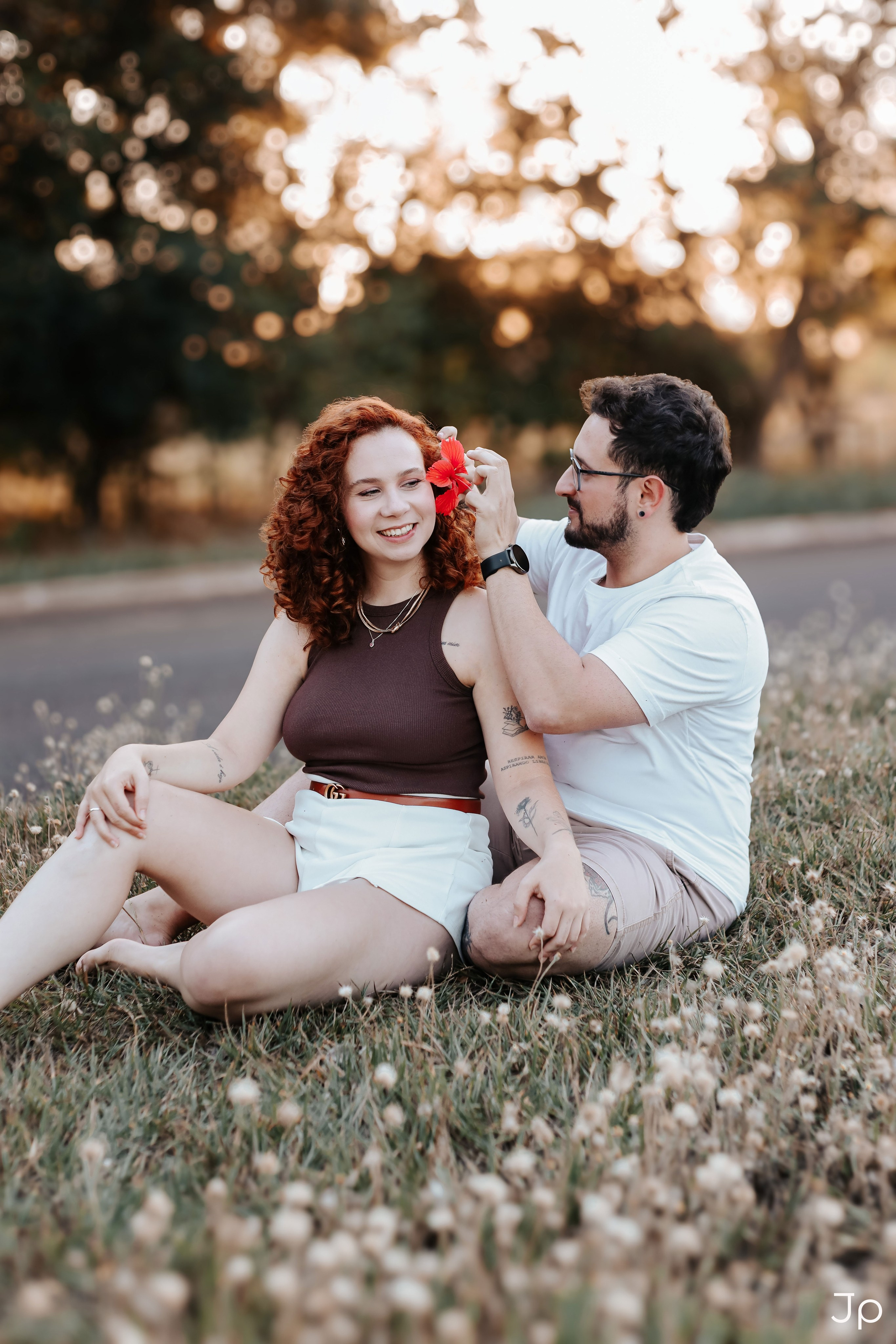 Ela segura uma flor vermelha, sentada de frente pra ele.