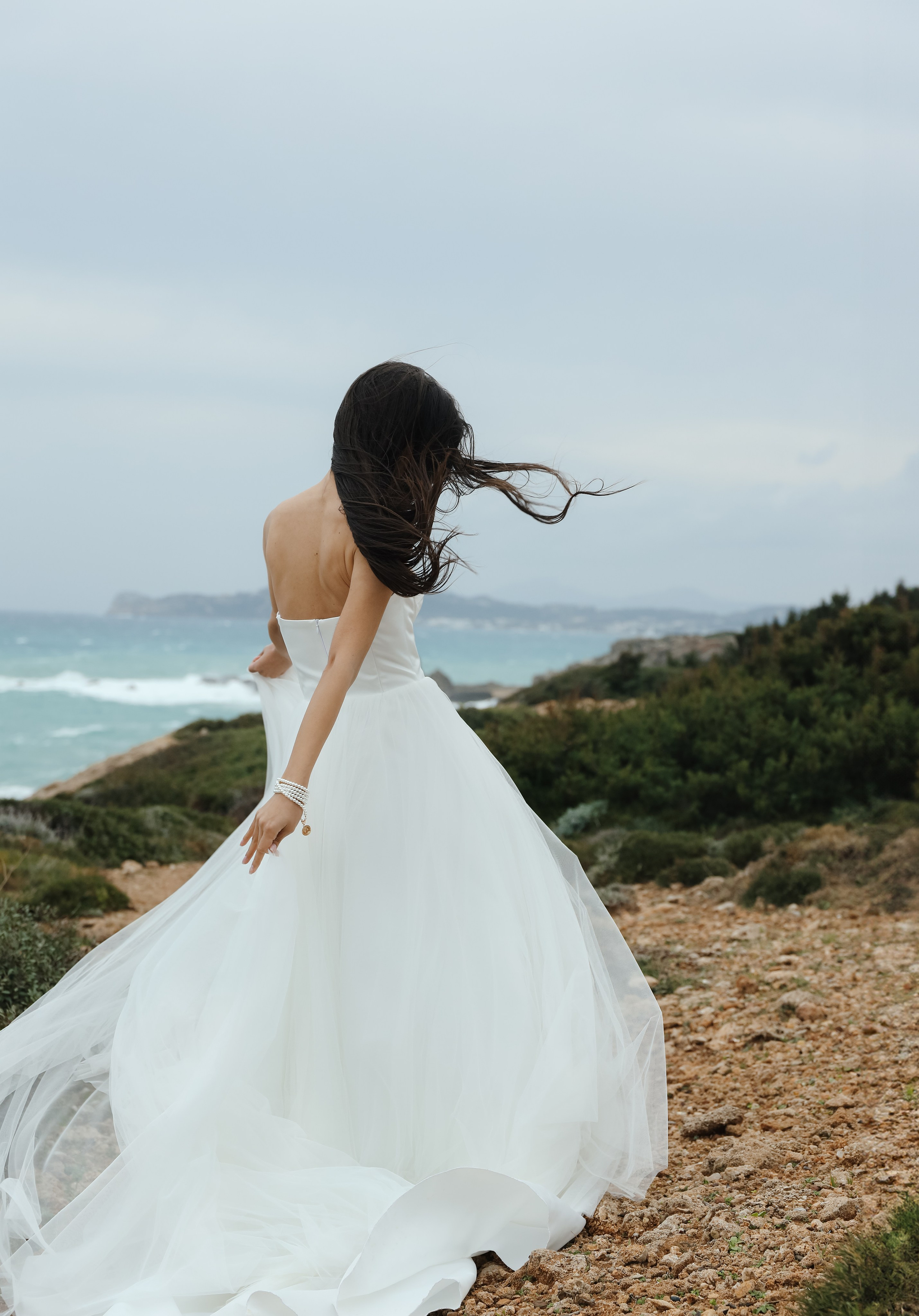 An art photo shoot of a girl in a wedding dress on the windy Kalithea beach in Rhodes, Greece