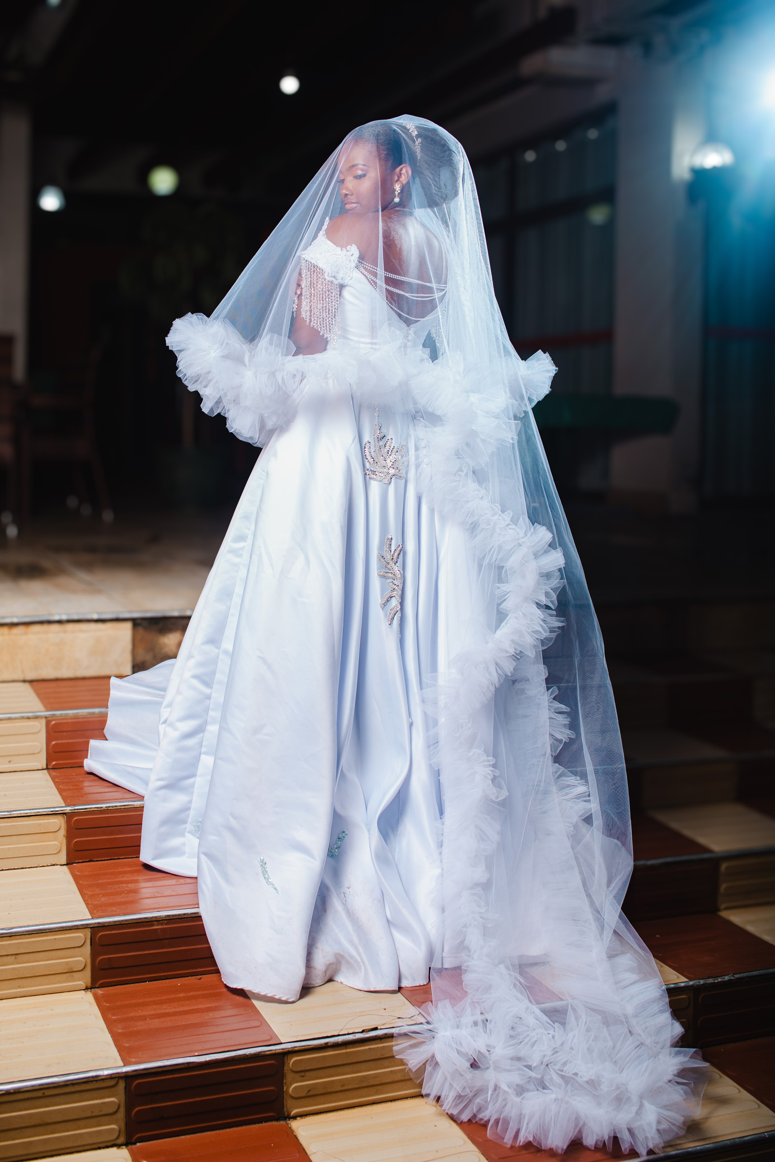 A portrait of a bride posing on a staircase, showing the full dress and details on her wedding day.