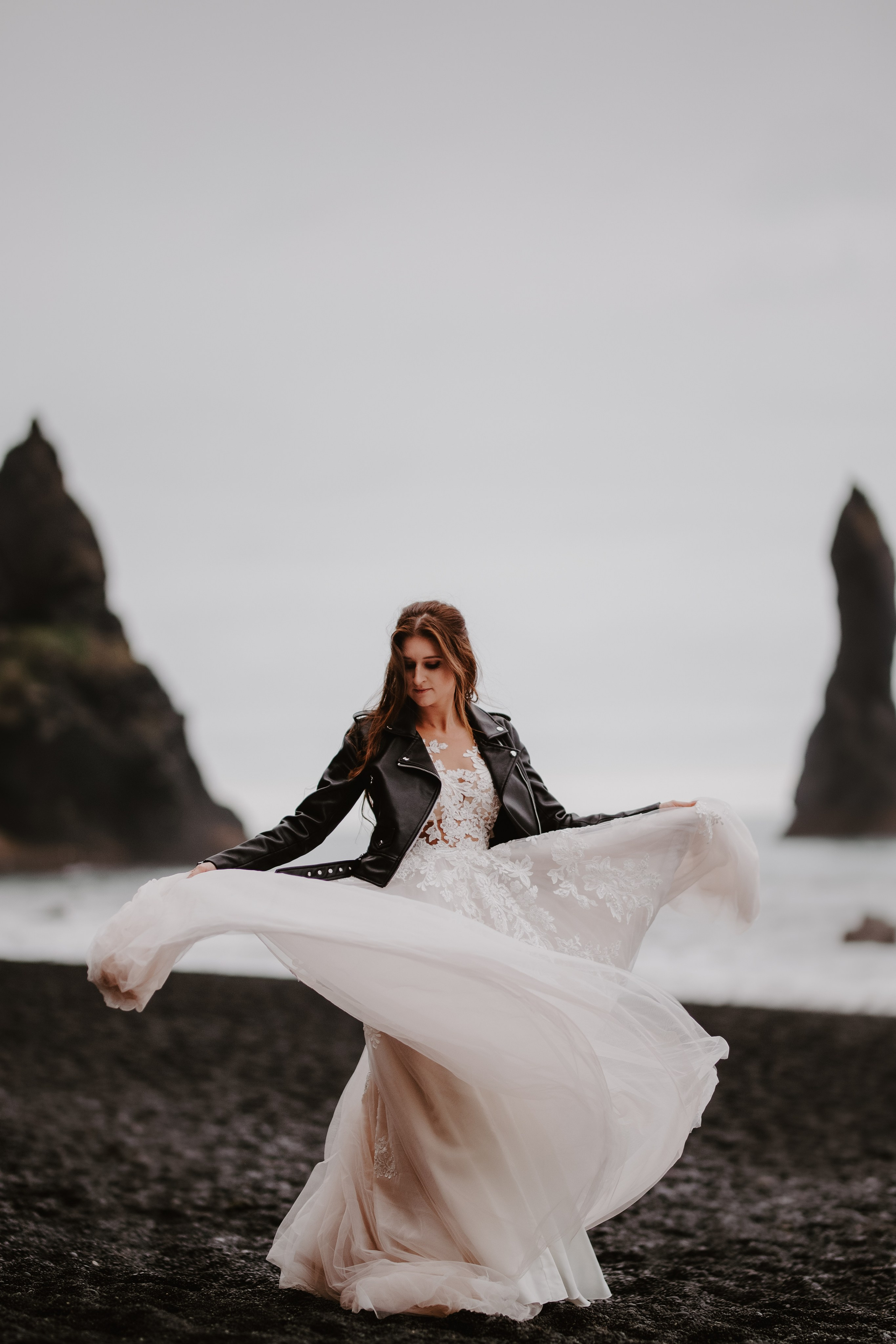 Love and adventure—couple walking along Reynisfjara Beach, Iceland, with the Reynisdrangar sea stacks in the distance.
