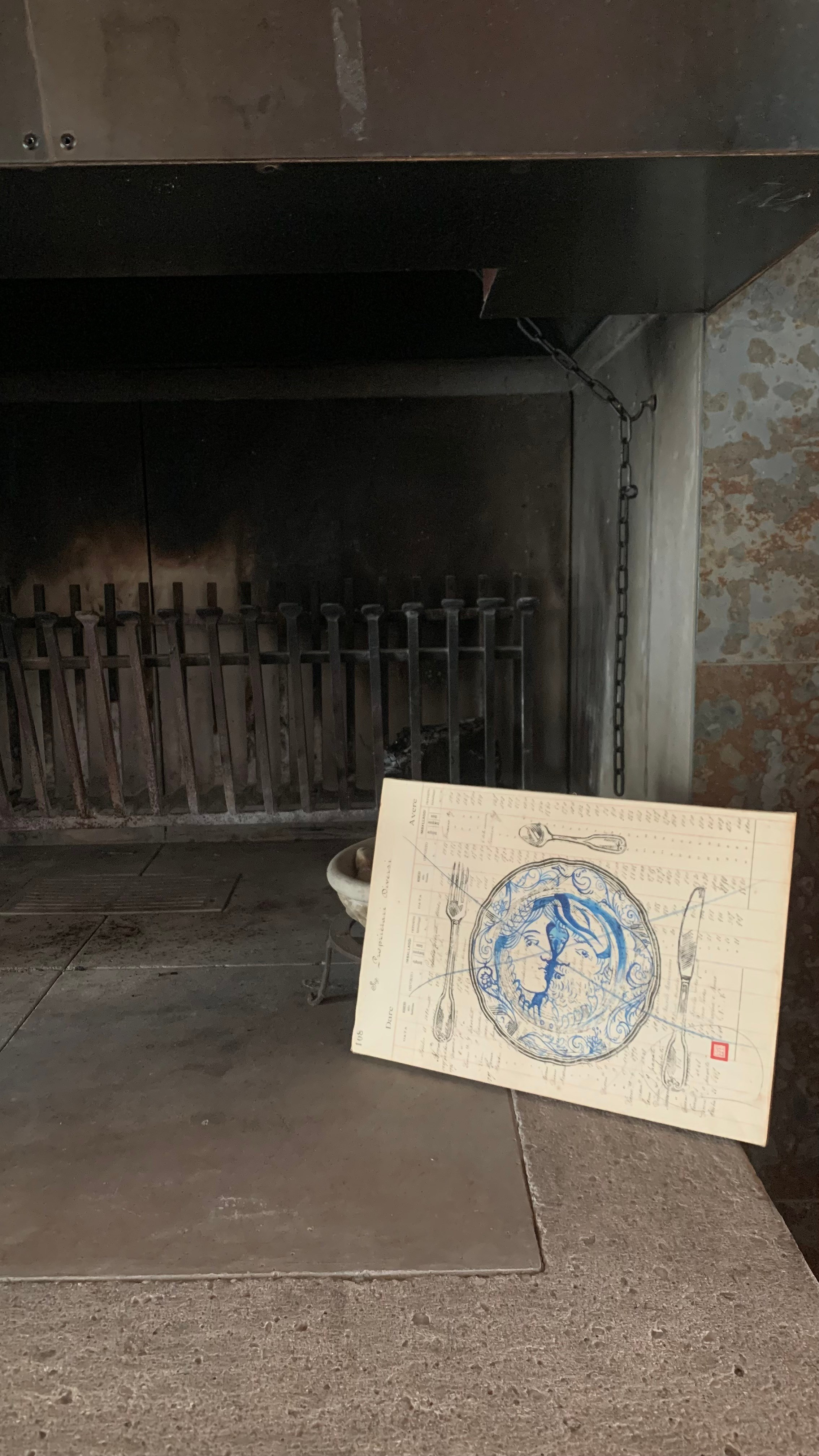 Opera su registro contabile storico (1918–1930) con stampa manuale in linoleografia. All’interno del piatto, un profilo umano dipinto in intenso inchiostro blu diventa fulcro visivo ed emotivo. Il blu dialoga con la carta antica e con il nero della stampa, evocando memoria, intimità e silenzio. Ispirazione ai piatti nuziali rinascimentali italiani, riletti in chiave contemporanea.