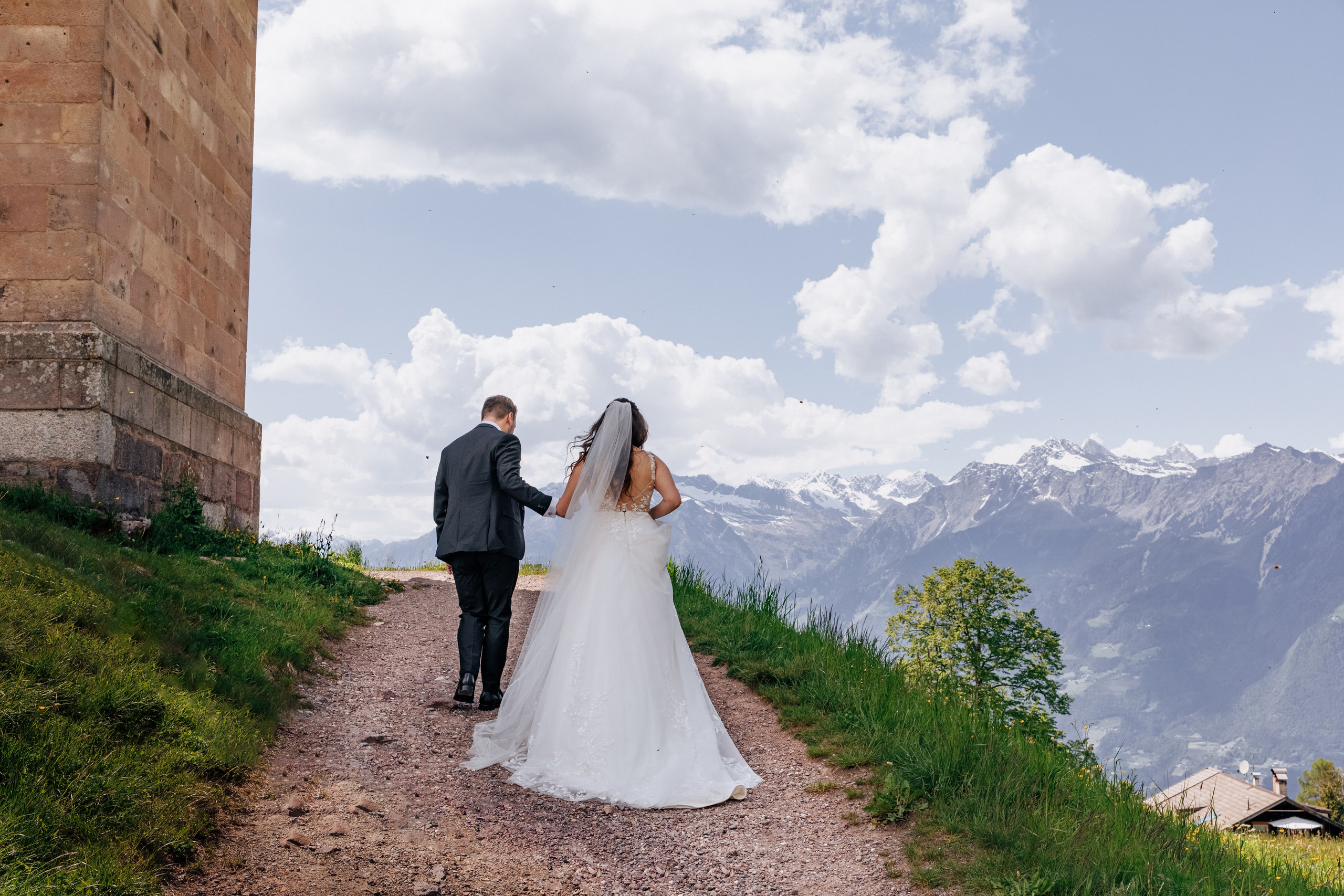 Der Bräutigam führt die Braut an der Hand vor der beeindruckenden Kulisse der Berge, ein romantischer Moment inmitten der Natur.