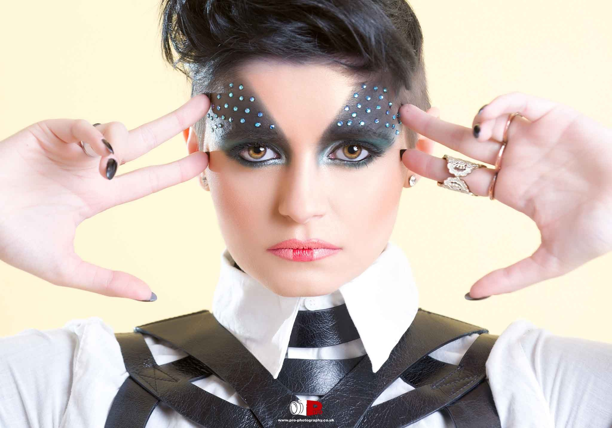 Creative fashion portrait of a model with bold makeup, rhinestones, and a unique leather outfit.