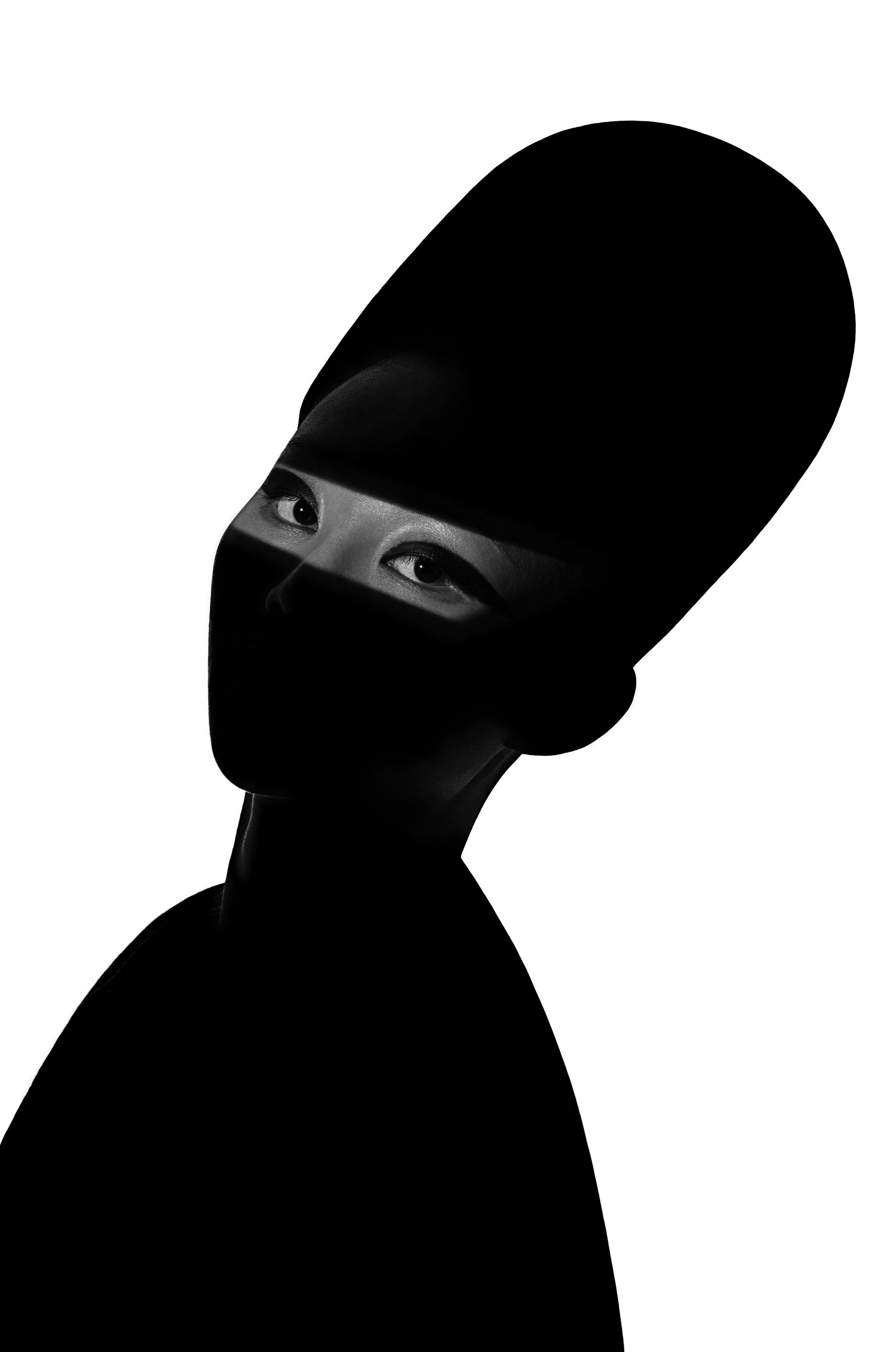 Singapore freelance photographer's high-contrast black-and-white editorial portrait featuring a female subject in avant-garde style. The image showcases a dramatic silhouette with illuminated eyes against a minimalist white background, perfect for modern fashion and creative branding in Singapore.