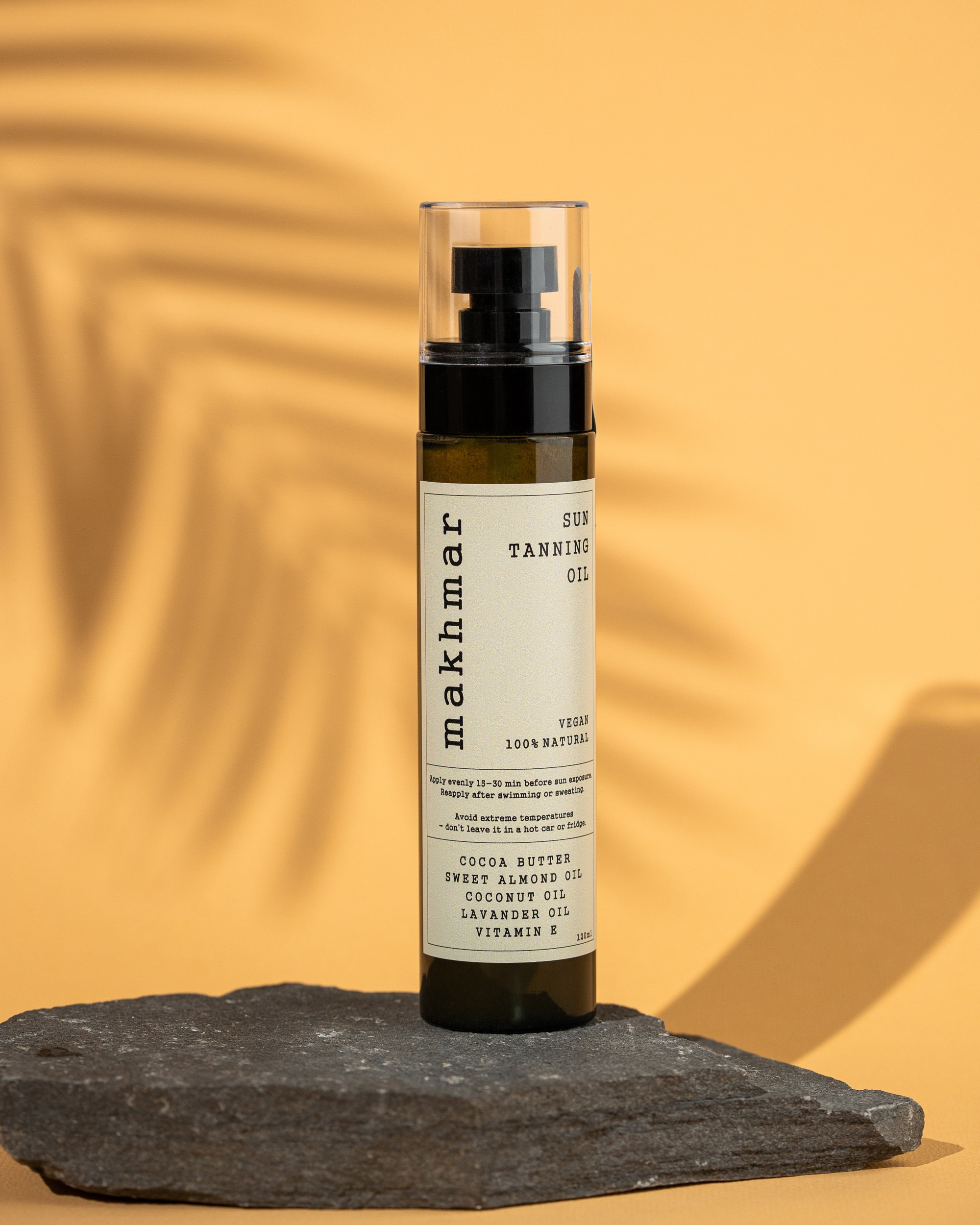 Makhmar Sun Tanning Oil şüşəsi, daş üzərində və kölgəli sarı fonda təqdimat.