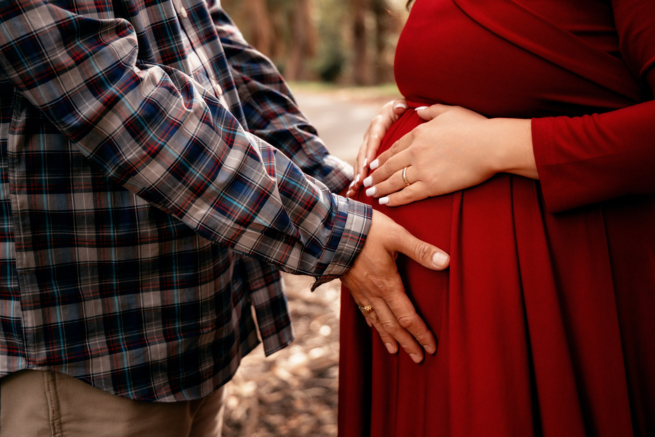 Joyful couple holding hands on the expectant mother’s belly with a forest backdrop
