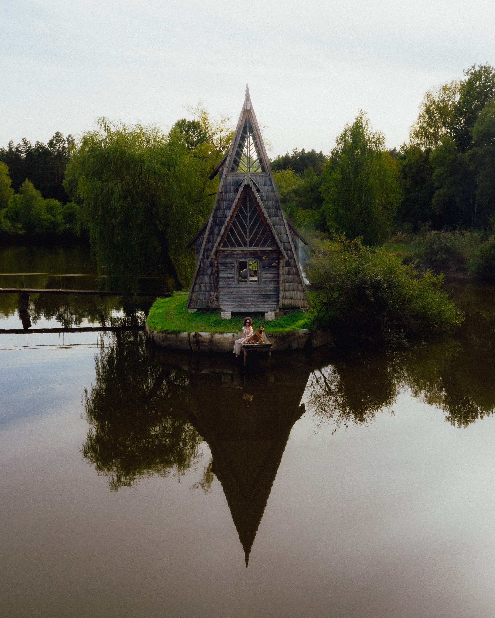A drone photo of a dog and a girl sitting next to a hut on a lake 