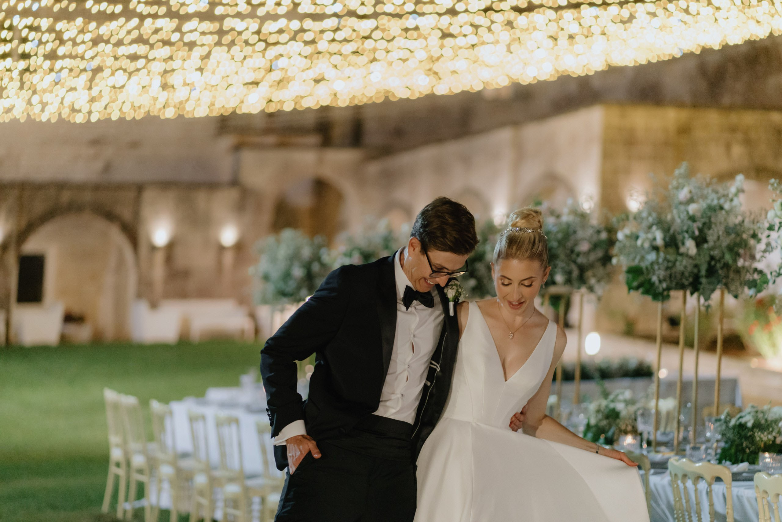Bride in flowing wedding dress walking with groom at night, atmospheric destination wedding photography in Ostuni Italy