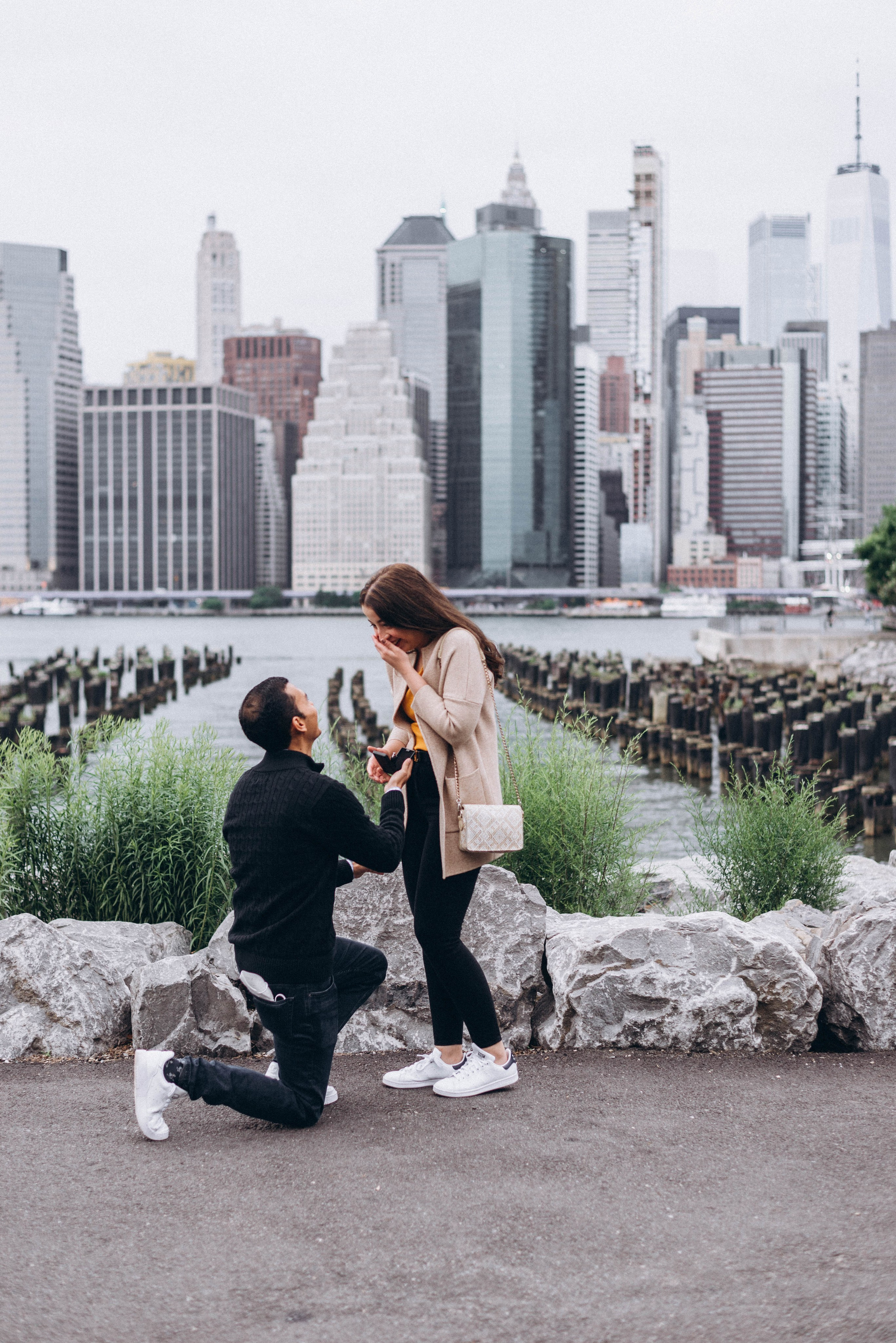 Man kneeling with ring in Dumbo cobblestone street.
