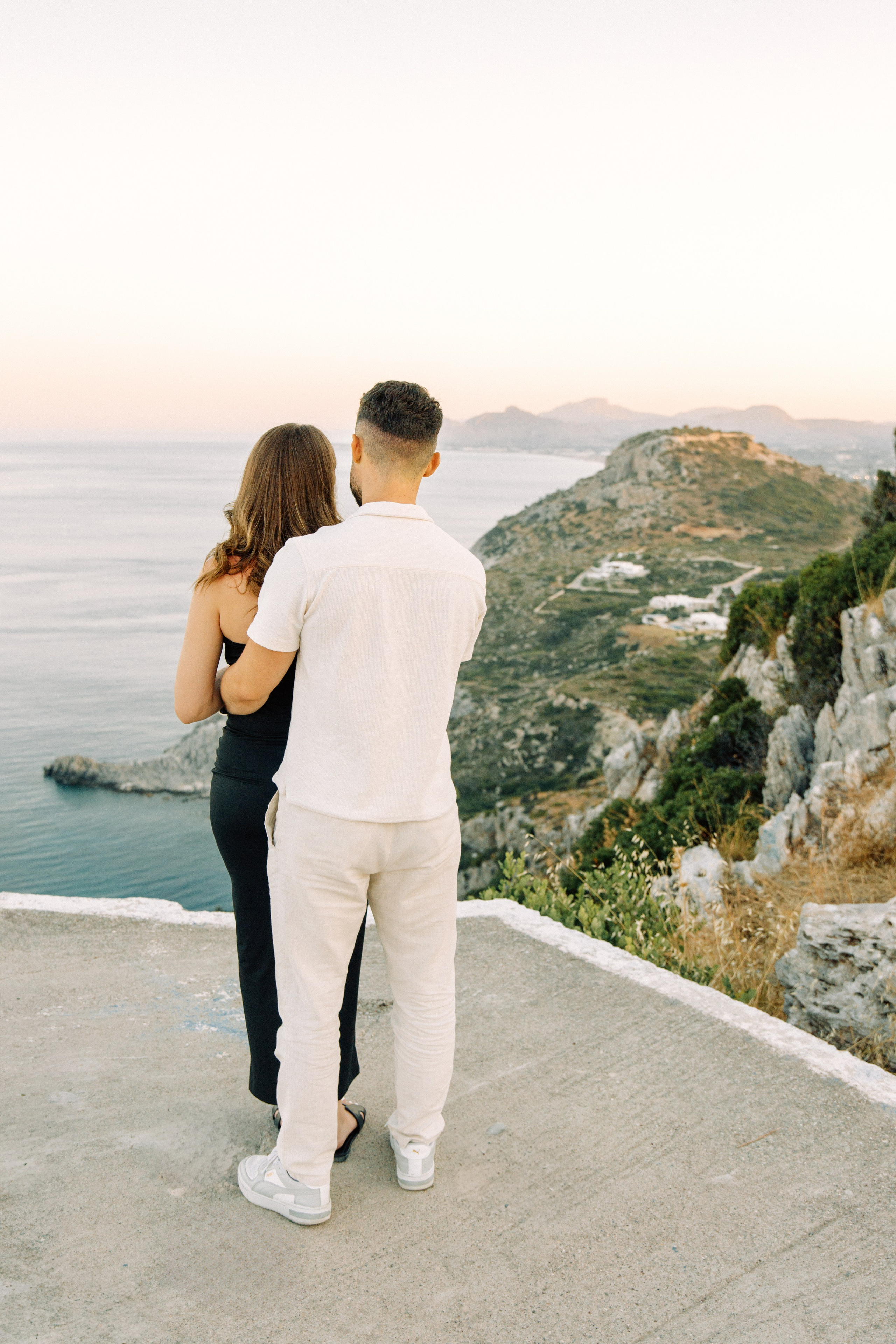 "Liebevoller Blickkontakt: Ein Paar auf dem Felsplateau des Profitis Ilias vor der Kulisse von Faliraki und dem Mittelmeer."