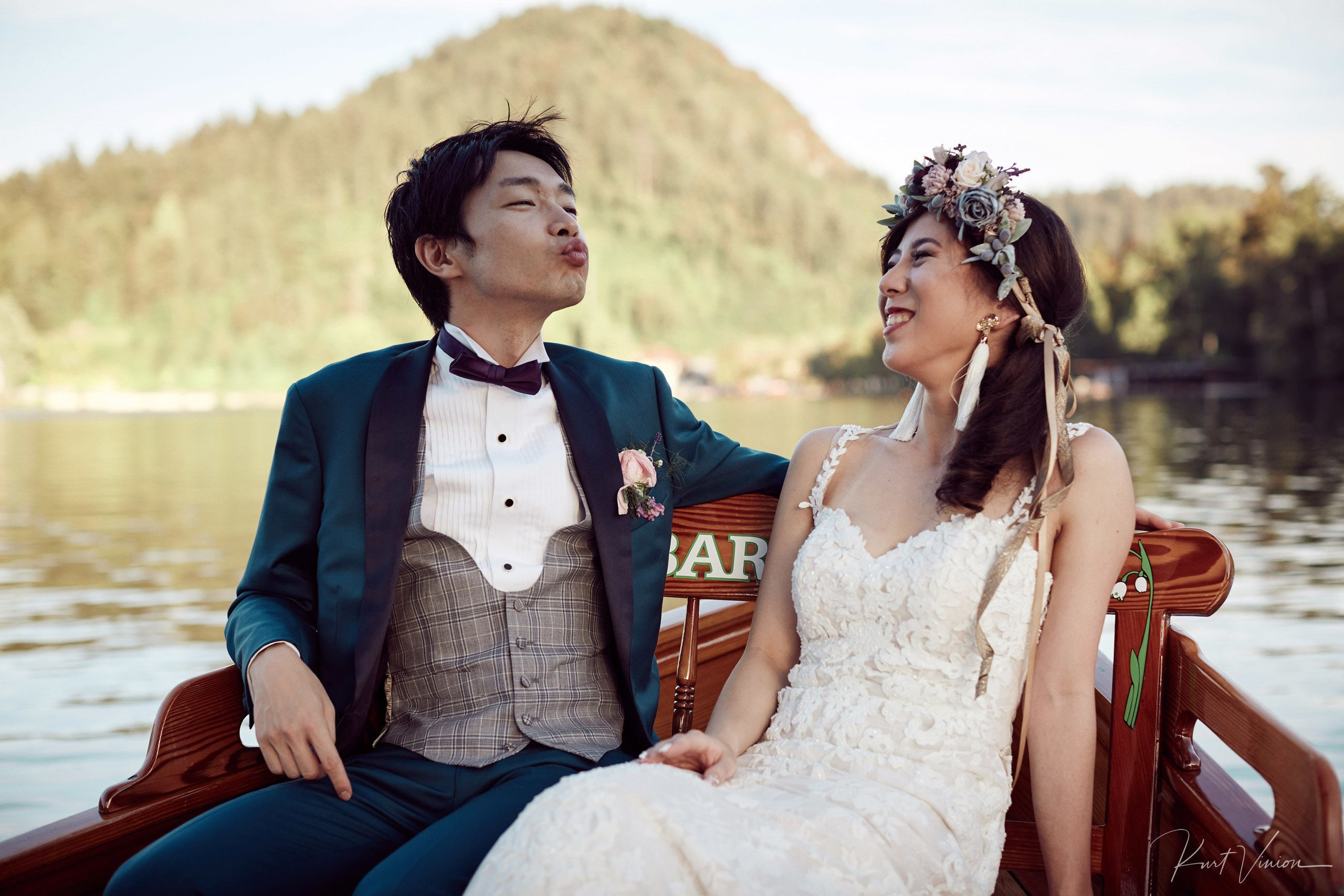 Newlyweds laughing joyfully crossing Lake Bled evening light.