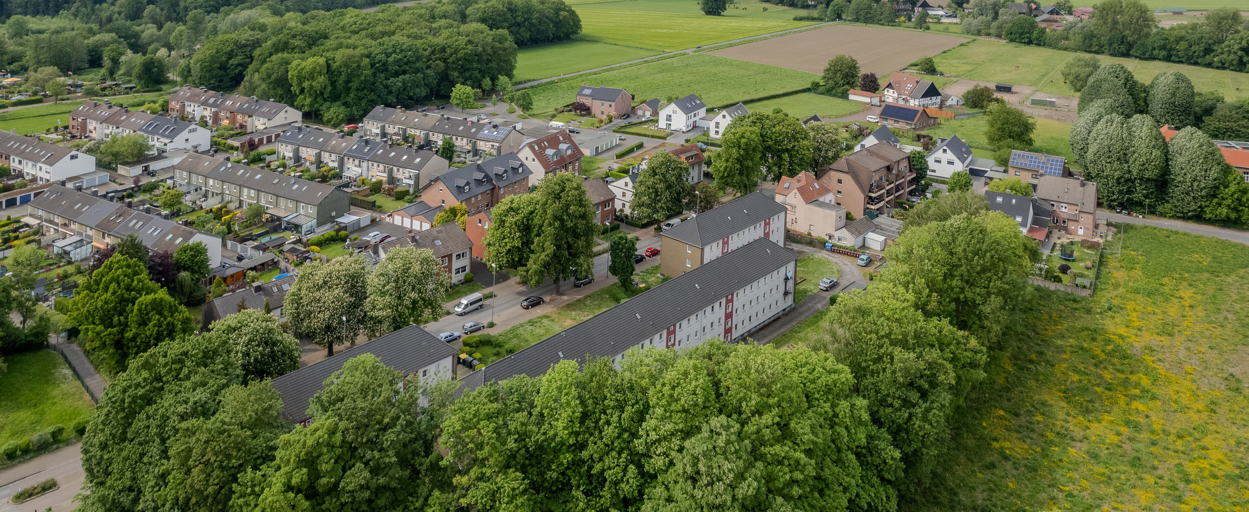 Аэрофотосъемка многоквартирного дома в HDR. Фасад, серая скатная крыша, земельный участок с зеленым газоном и подъездной дорогой. Панорамный вид с высоты, сделанный с помощью дрона.
