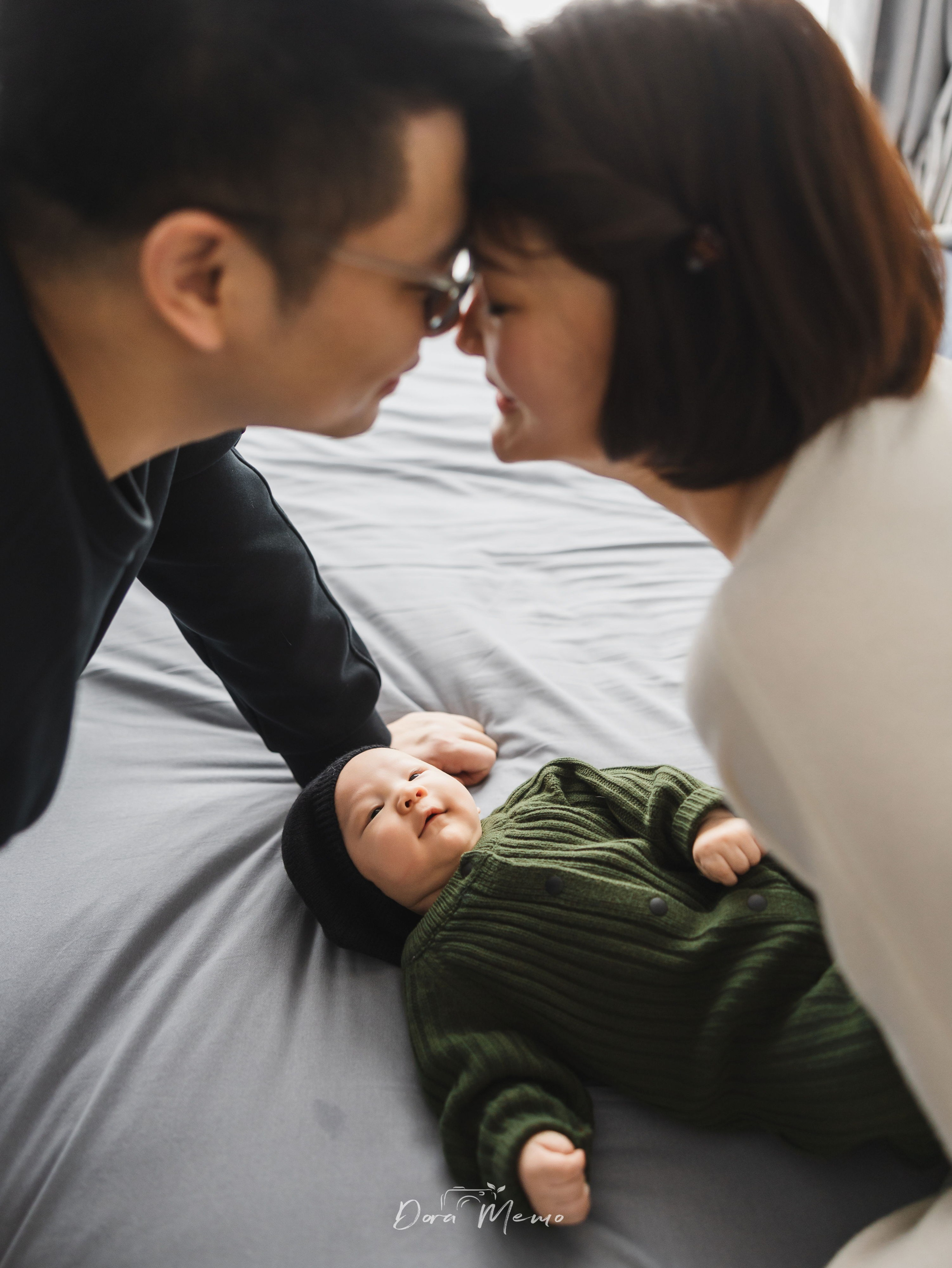 Parents leaning close to baby lying on bed, intimate family interaction at home