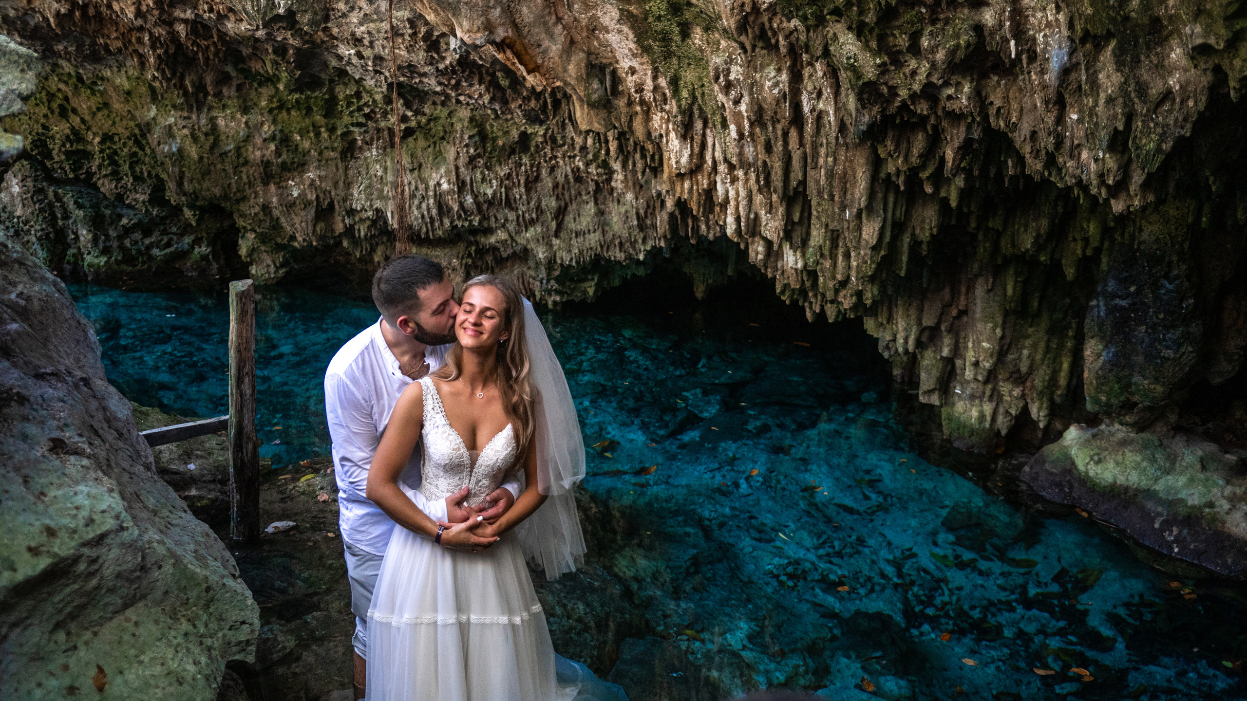 Groom embracing bride by crystal-clear water in Tulum
