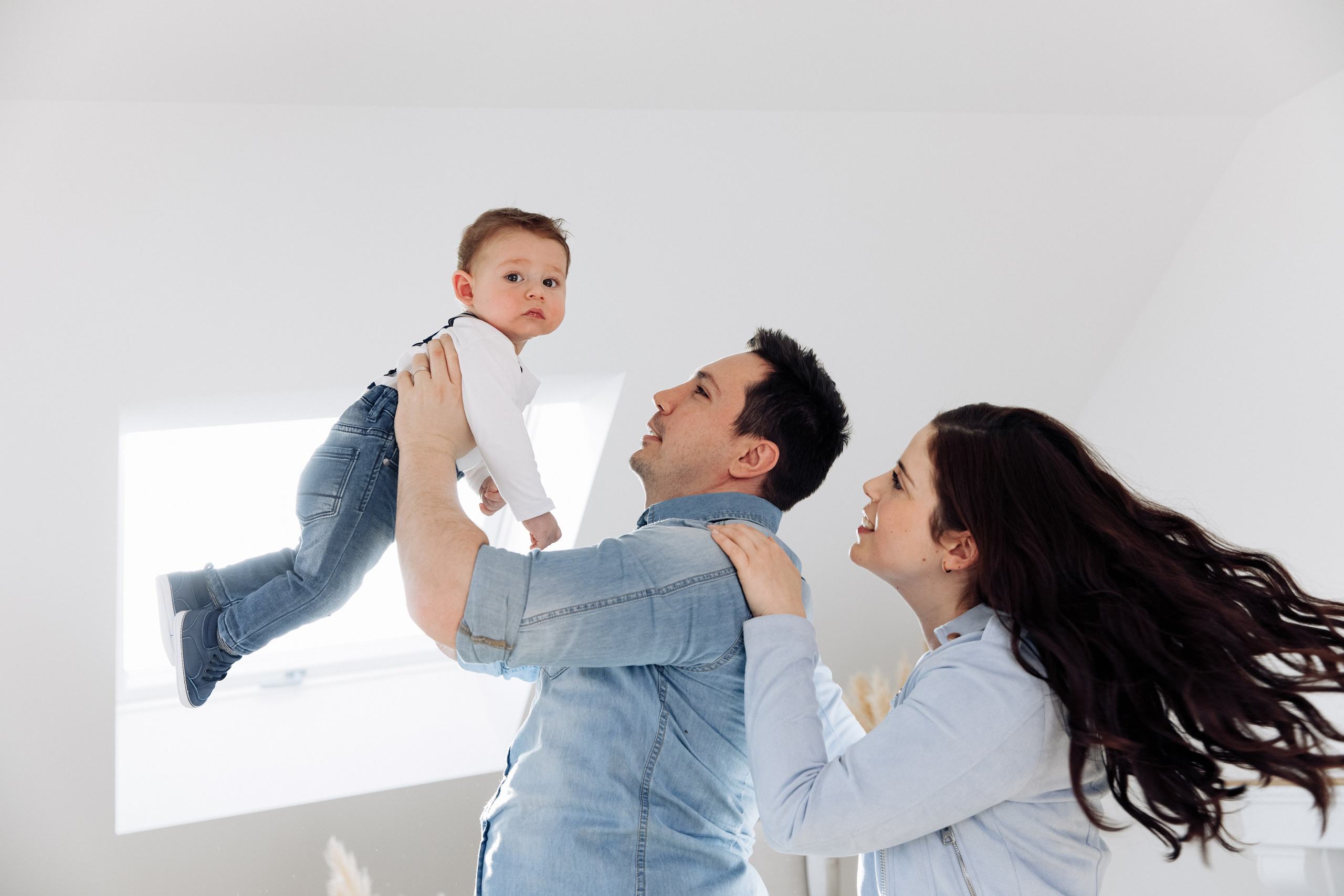 Vater und Mutter werfen während des Fotoshootings im Studio ihren Sohn hoch in die Luft.