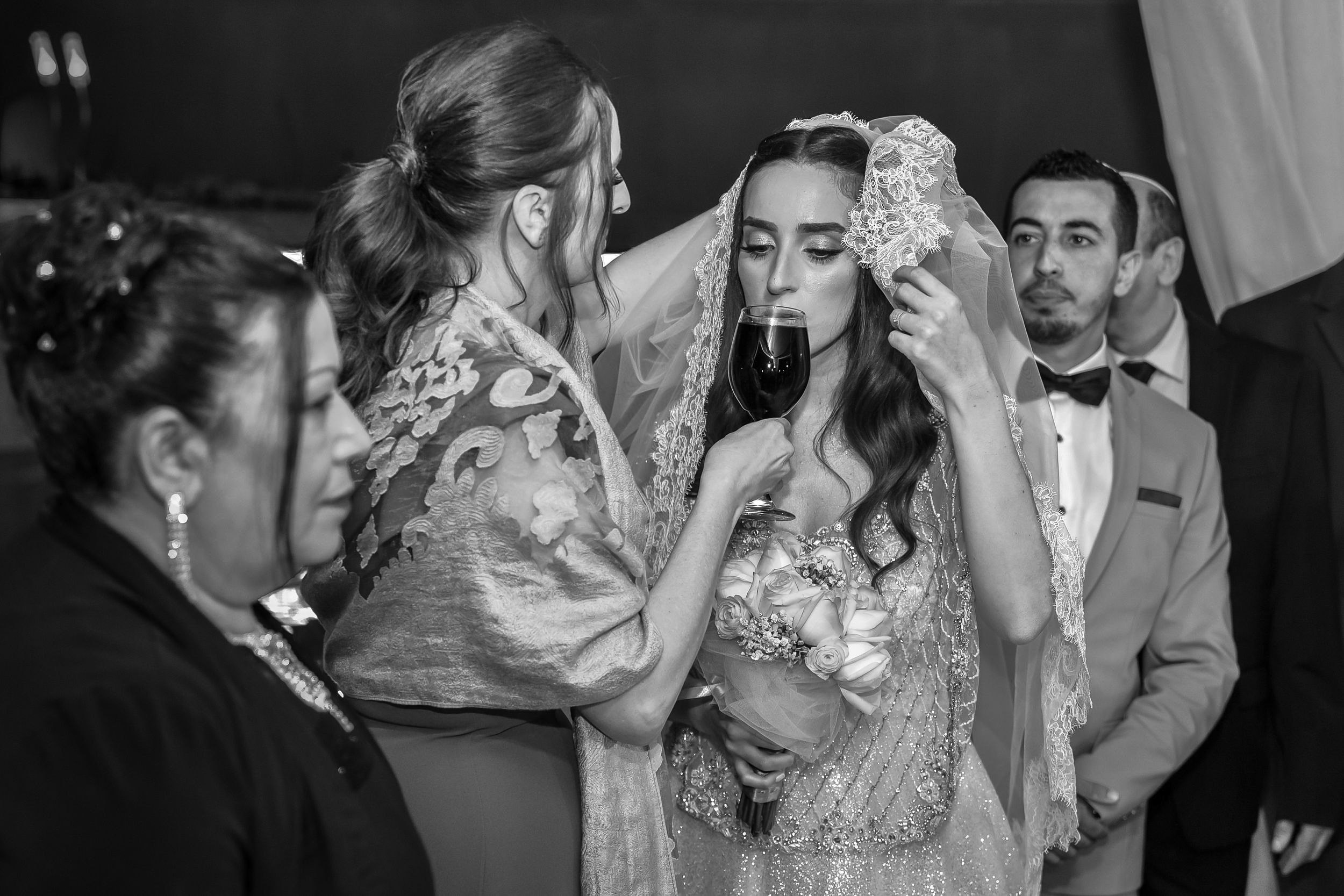 Dana drinks from a wine glass held by her mother beneath the chuppah