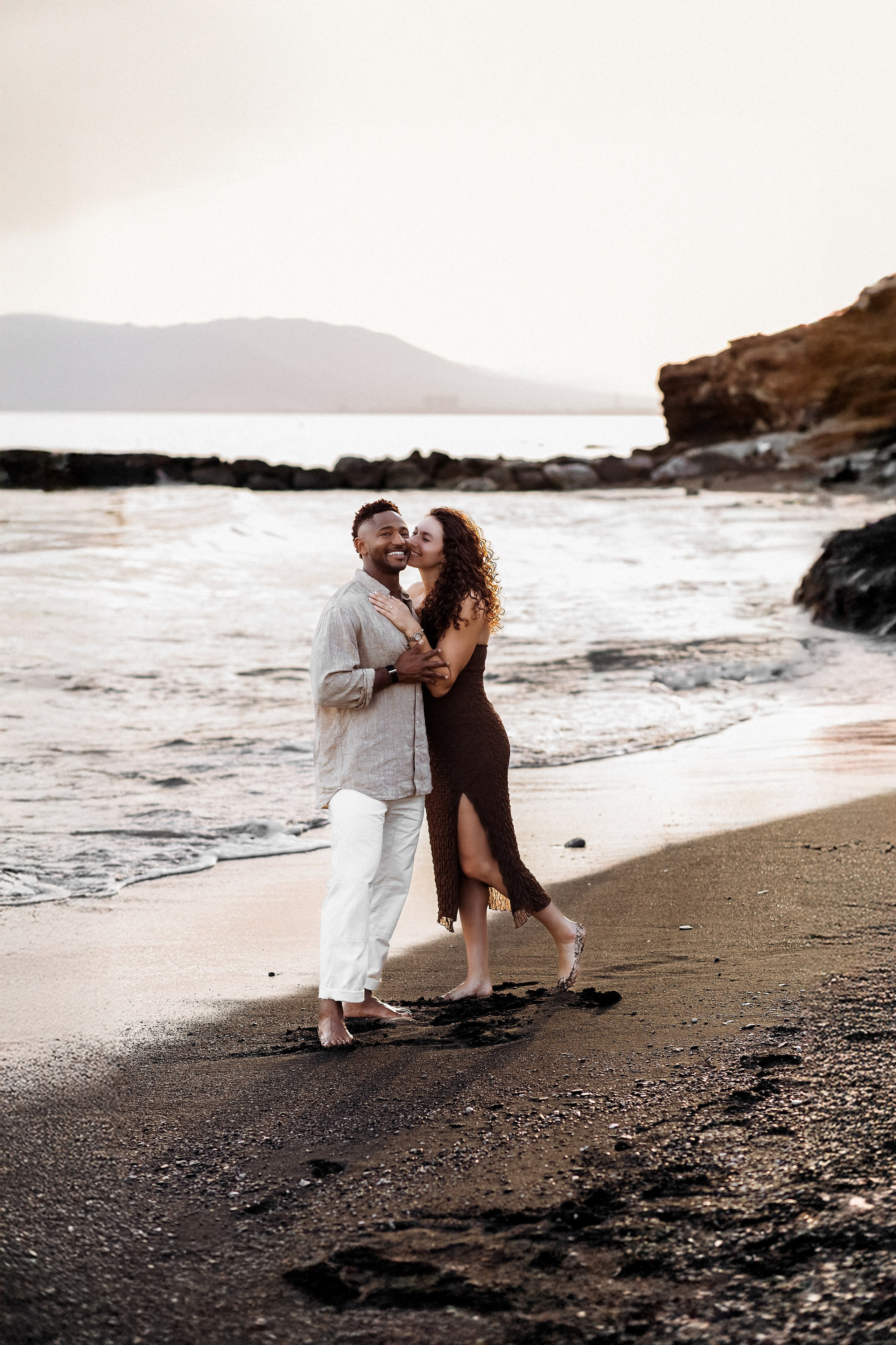 Intimate embrace during a destination engagement session on a Málaga beach following a romantic seaside proposal. Candid proposal photography highlighting movement, waves, and timeless black-and-white storytelling.