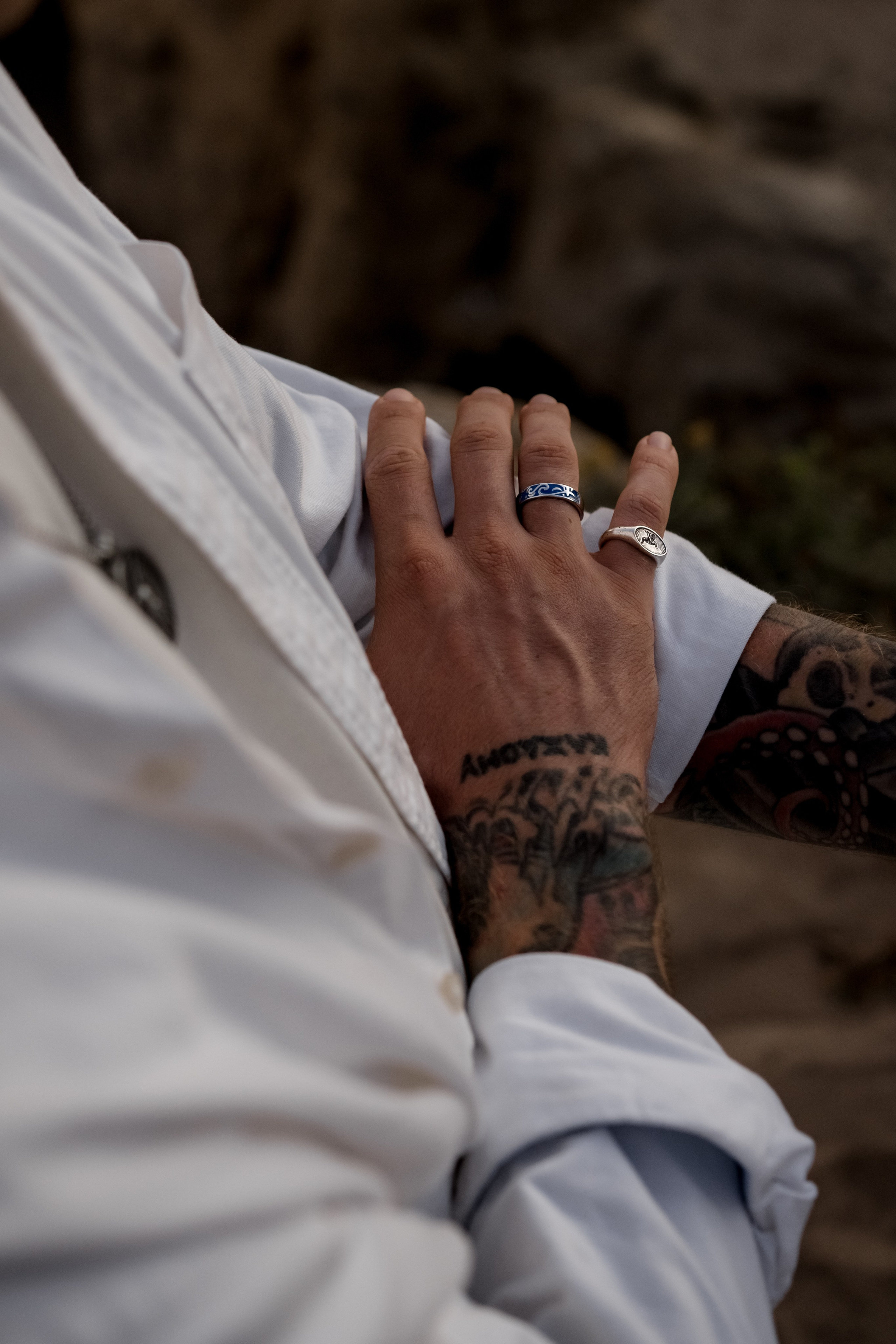Tattooed hands adjusting a silver bracelet, captured against a natural rocky background.
