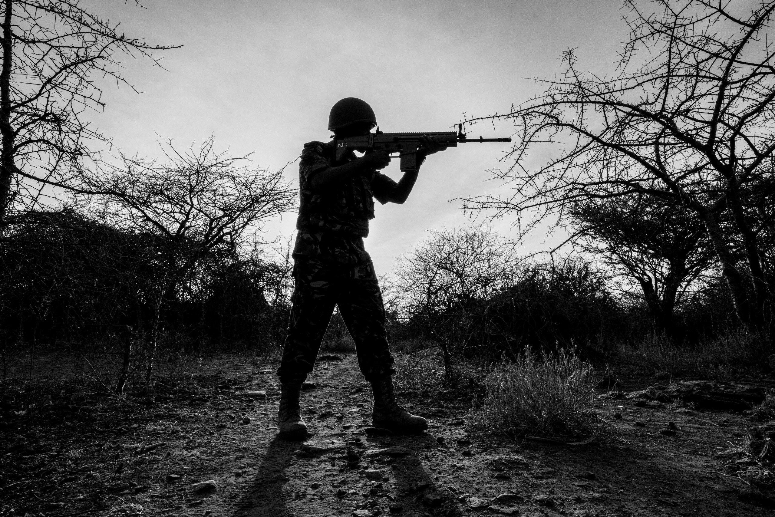 A Silhouette full shot of a soldier in combat position, in an arid area. Documentary photography