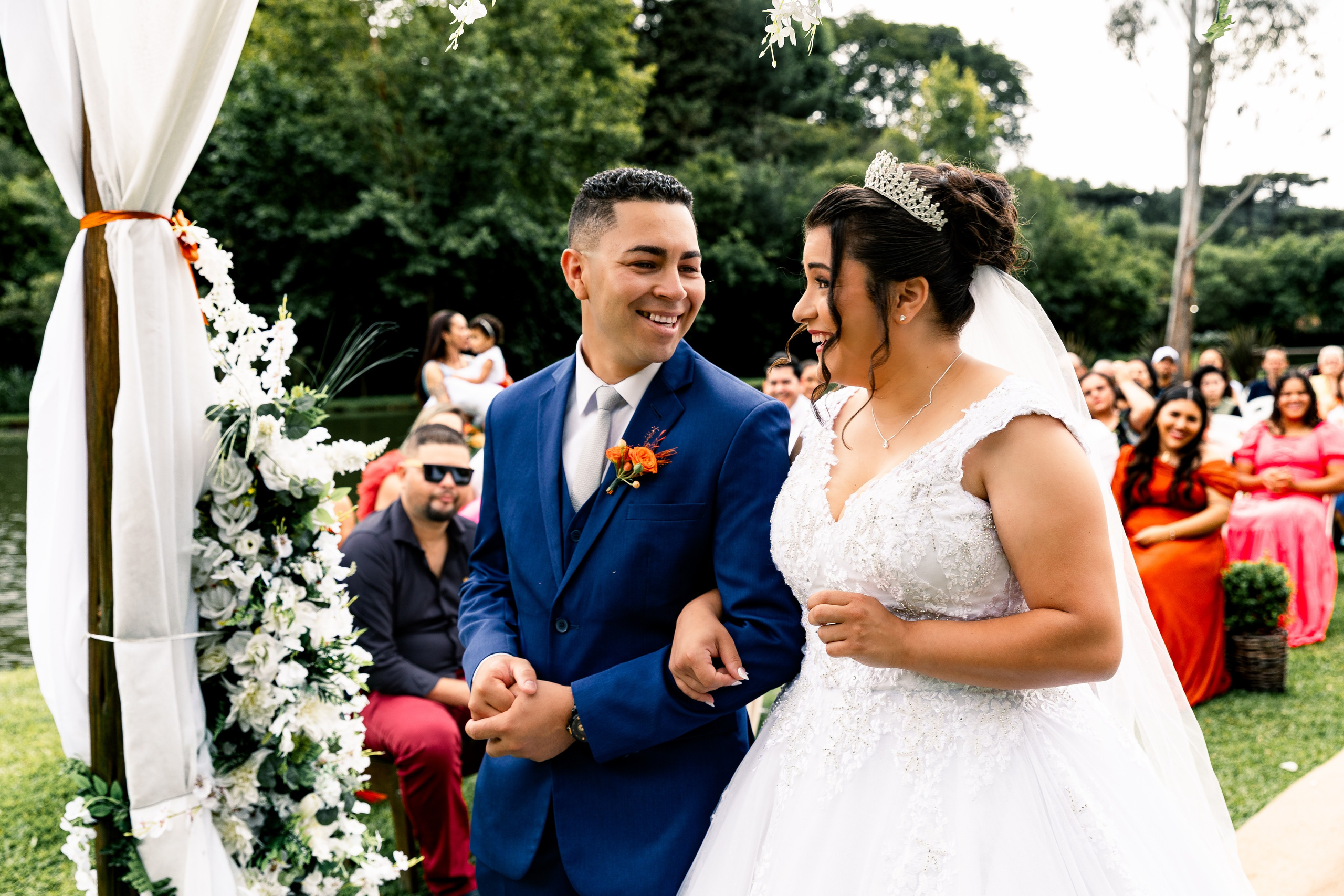 Noivos sorrindo juntos em frente ao altar decorado com flores, celebrando o início da nova jornada.