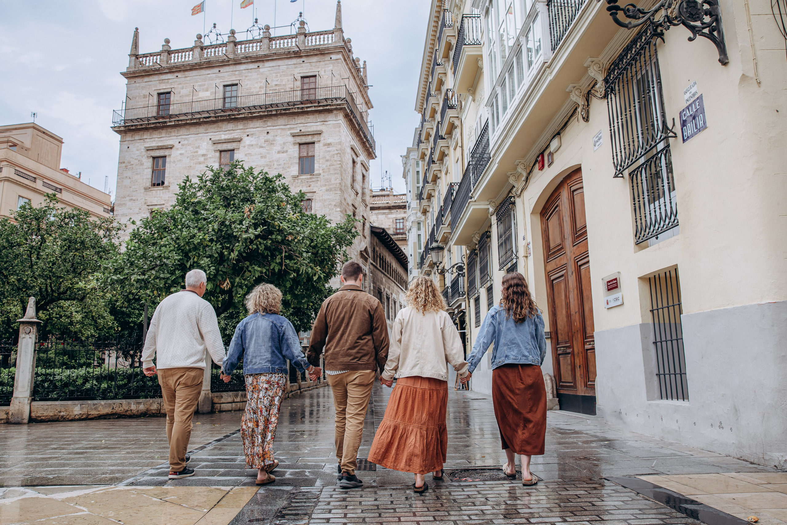 Familia multigeneracional caminando de la mano por las encantadoras calles históricas de Valencia, España durante una sesión familiar espontánea. Inspiración ideal para quienes buscan sesiones familiares en Valencia y sesiones lifestyle auténticas en España.