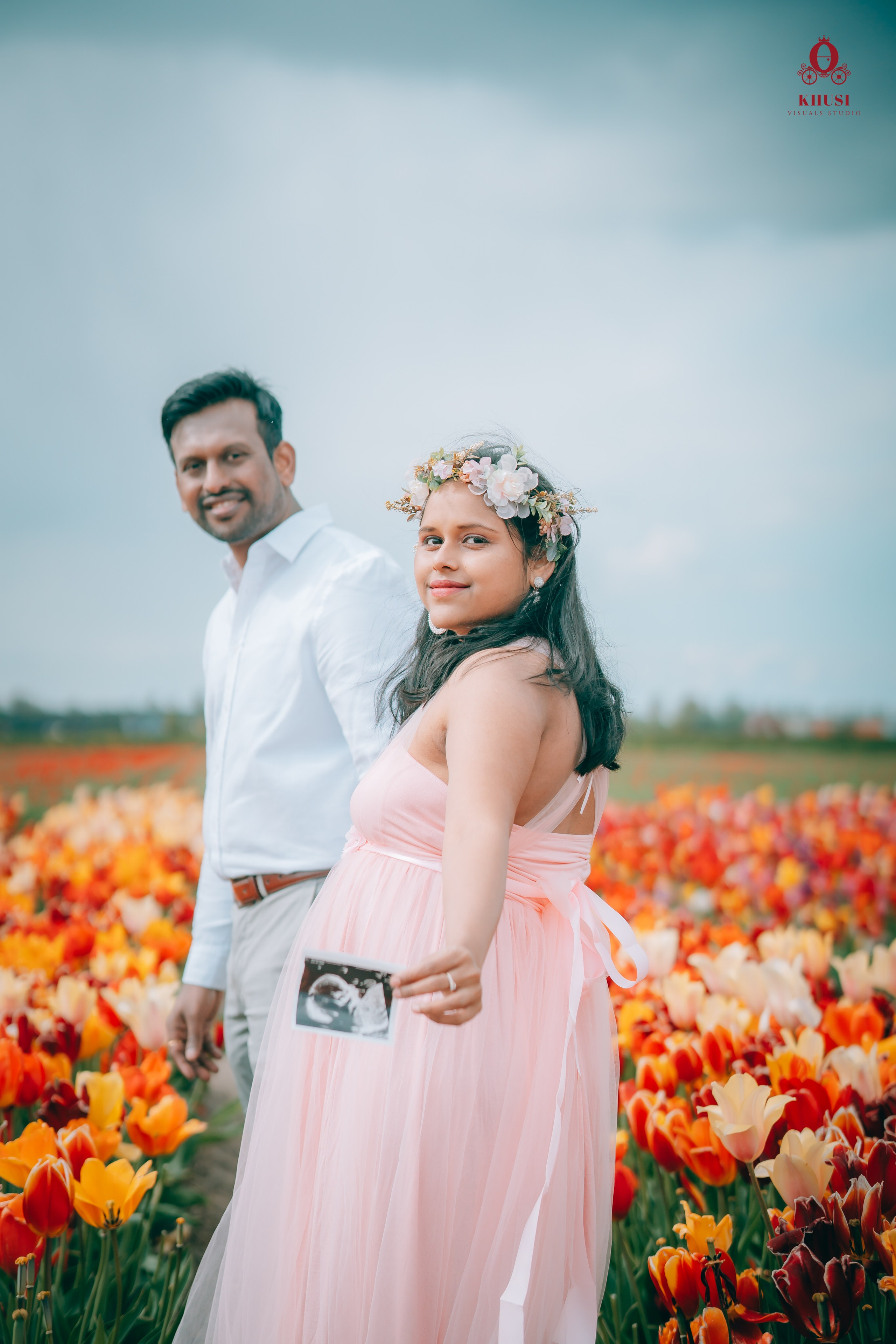 a couple holding the sonogram of their baby and walking in tulip fields in Netherlands