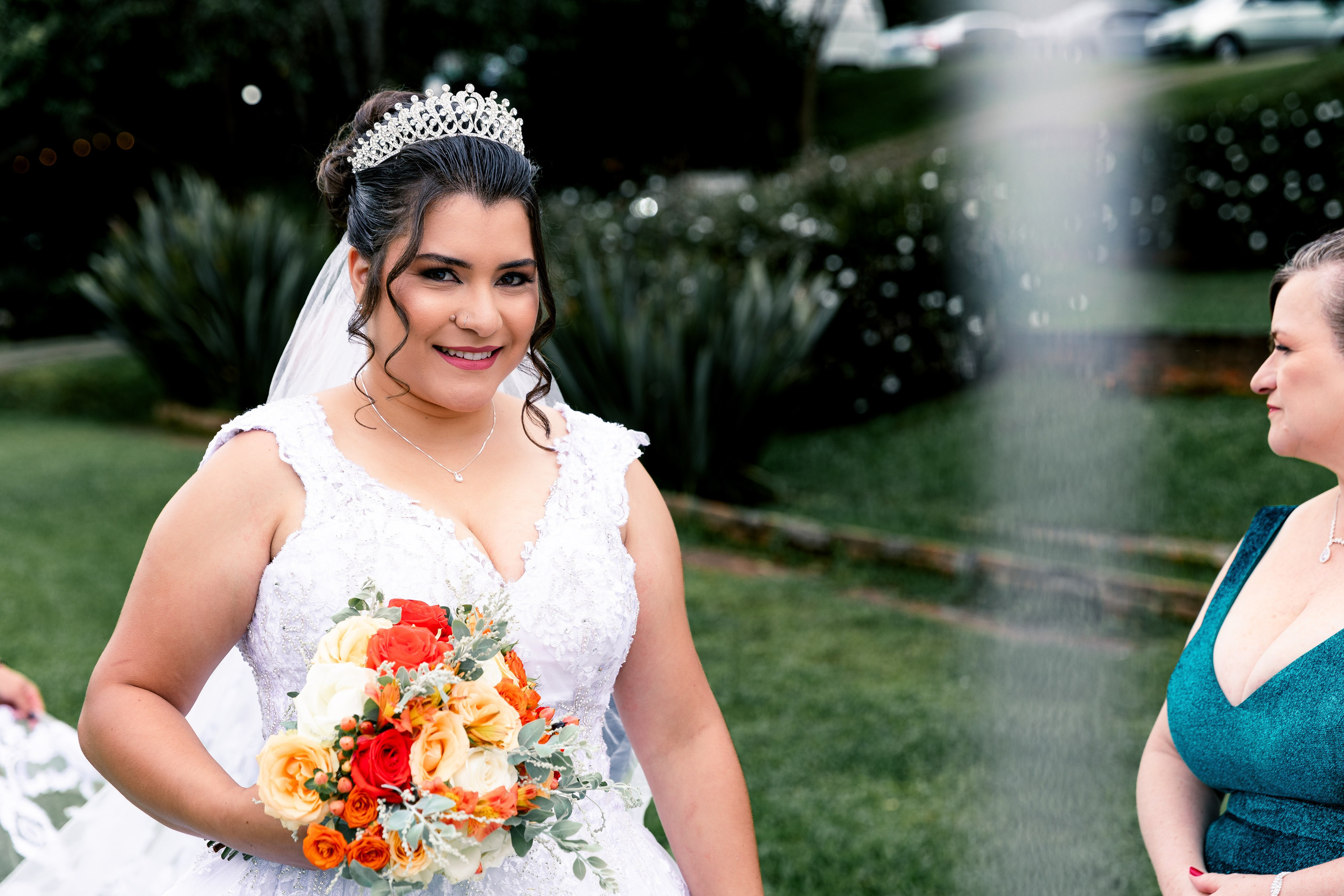 Noiva sorrindo com buquê nas mãos ao lado da mãe, momento de alegria antes da entrada.