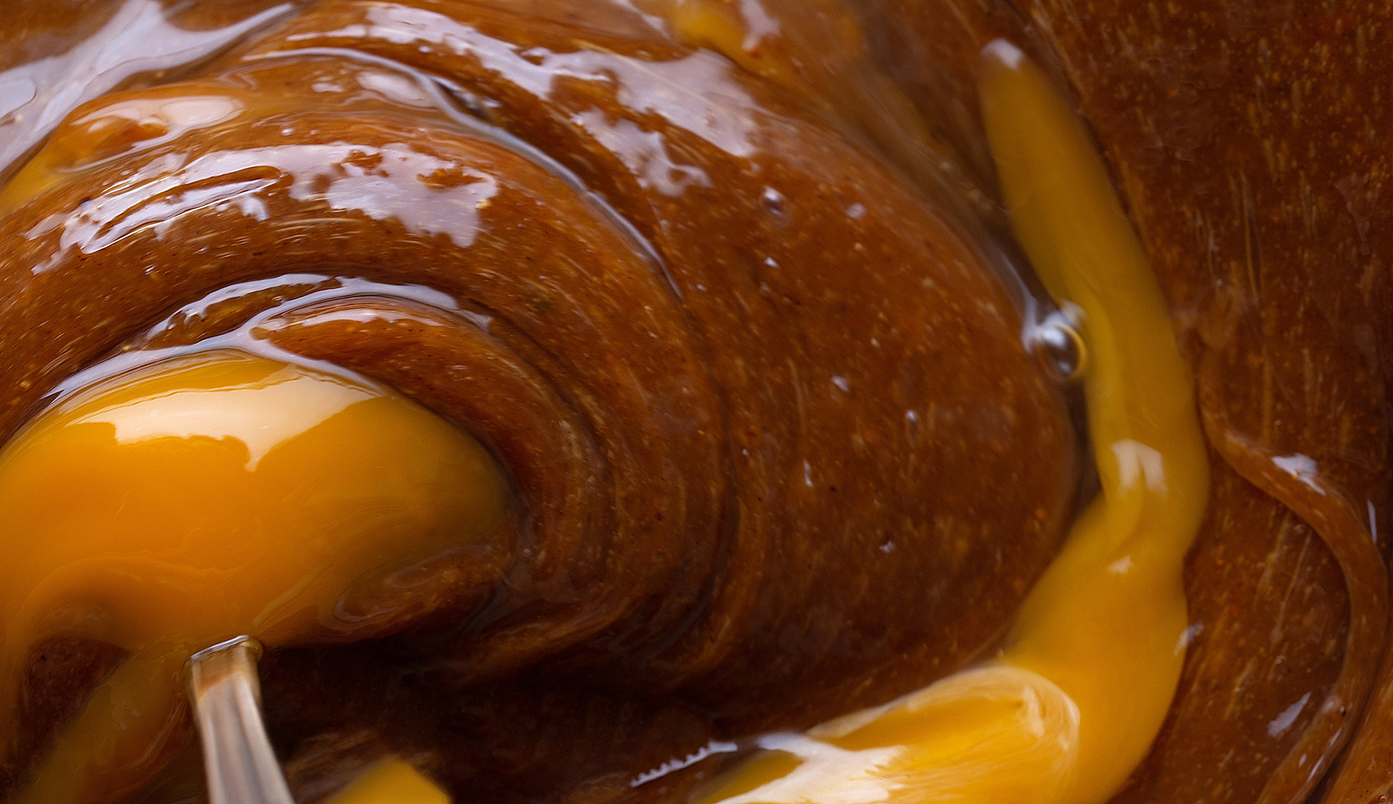 close-up of egg yolk being mixed into thick brown dough, creating a rich, smooth texture