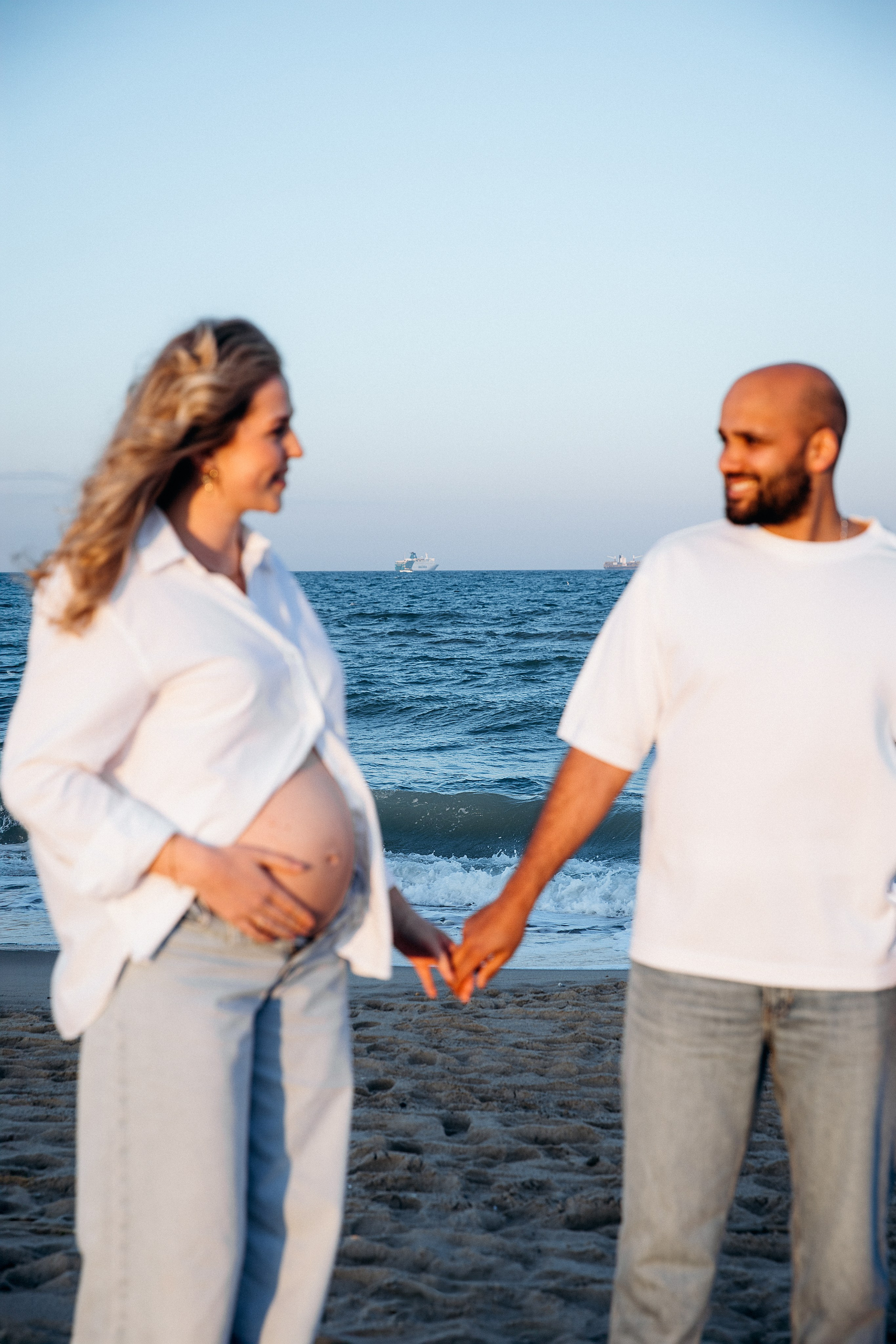 Sesión de fotos de embarazo en Valencia, España, con una mujer embarazada en una pose relajada con un suave fondo costero, creando un retrato natural y lifestyle — ideal para sesiones de embarazo y maternity en Valencia y en toda España.