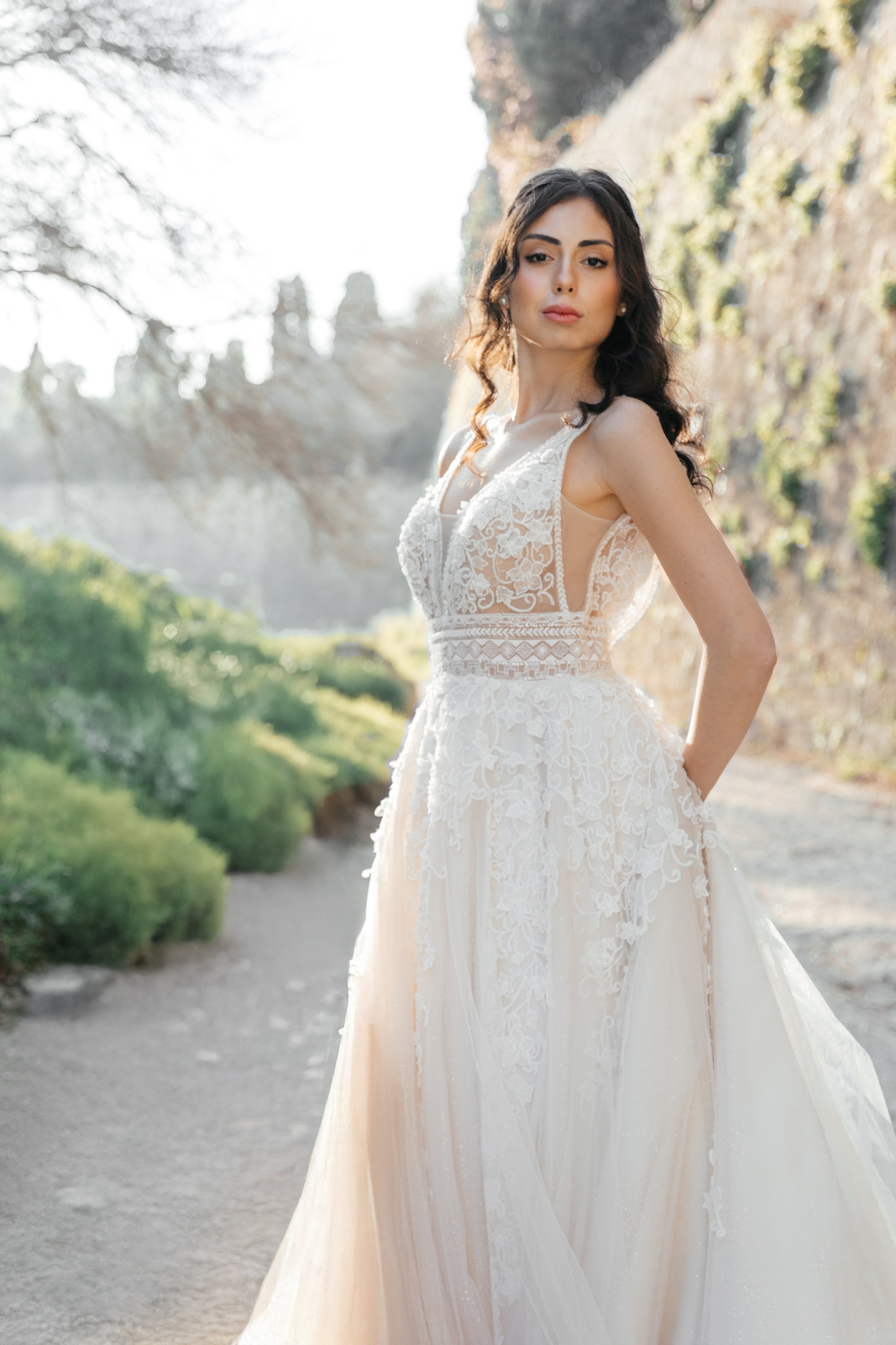 A stunning bride gazes thoughtfully in the enchanting alleys of Rhodes' Old Town, her flowing wedding dress complementing the rustic charm of the cobblestone streets and ancient architecture. The editorial-style portrait captures her poise and the romantic atmosphere of the medieval surroundings, bathed in warm, golden light.