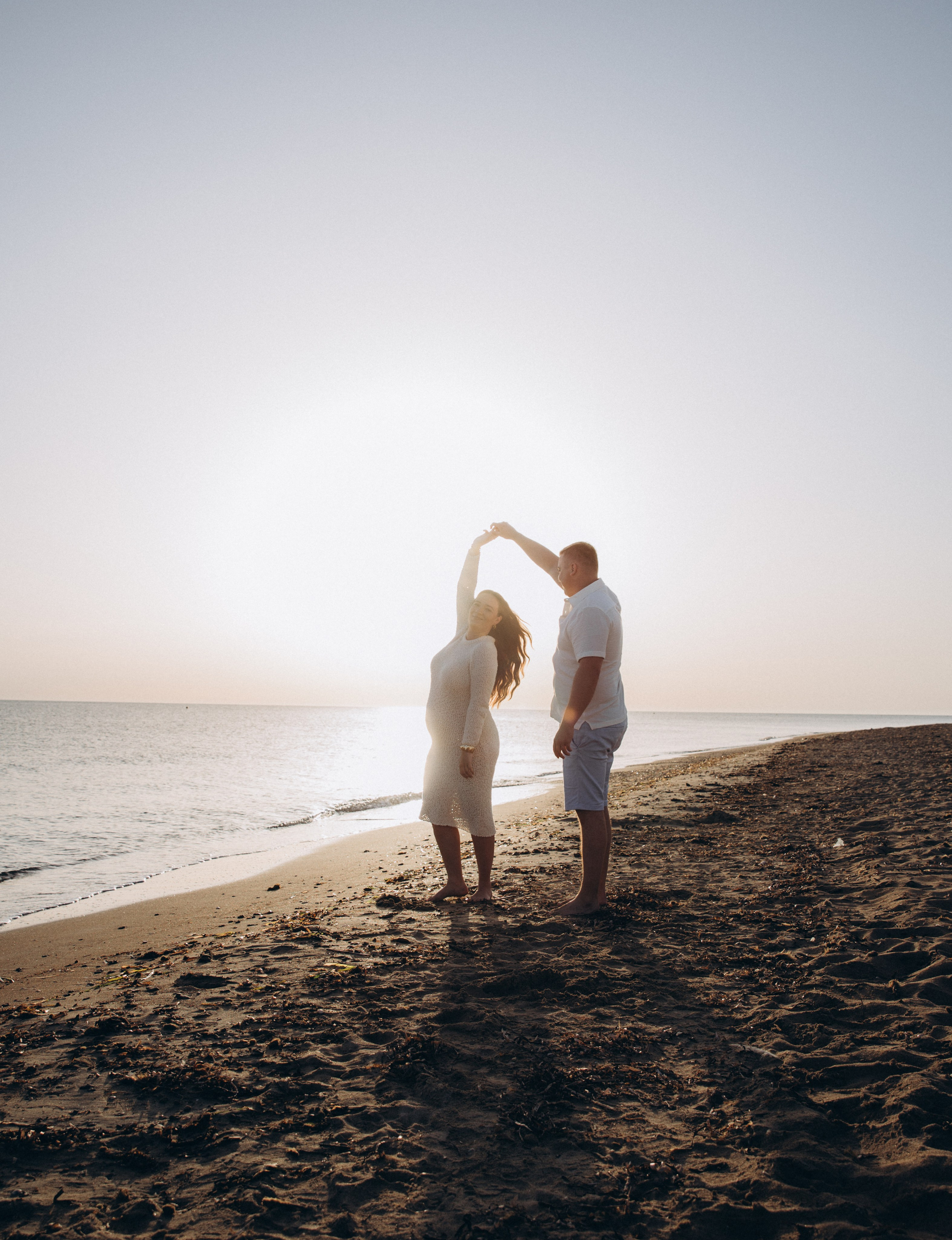 Romántica sesión de embarazo en la playa de Alicante, España — pareja bailando al atardecer junto a la orilla, capturando el amor, la anticipación y la belleza del mar Mediterráneo.