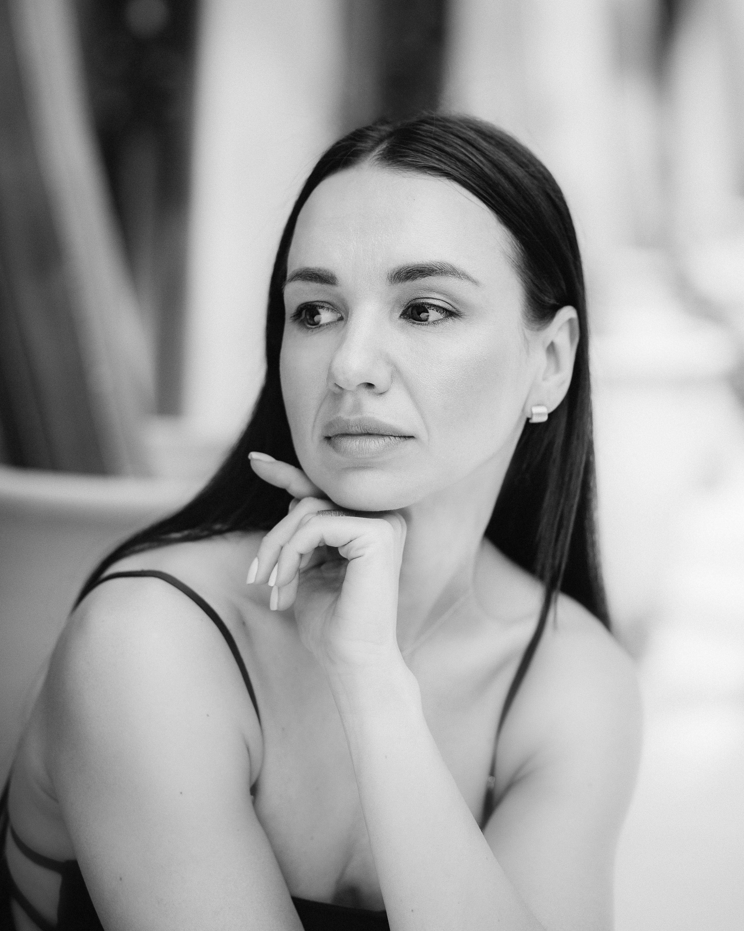 Задумчивая женщина с гладкими волосами, опирающаяся подбородком на руку, в мягком черно-белом крупном портрете, снятом в Барселоне, Испания — элегантная и минималистичная портретная фотография, подчеркивающая вечную красоту и эмоциональную глубину, идеально подходит для портретных фотосессий в Барселоне и Испании.