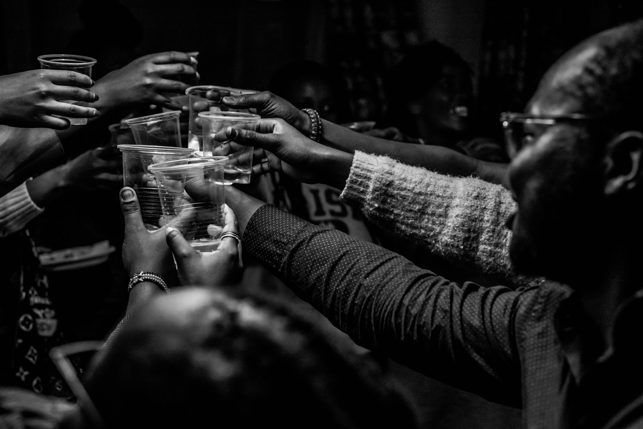 A high contrast black and white photo of several hands toasting during a birthday event in Nairobi.