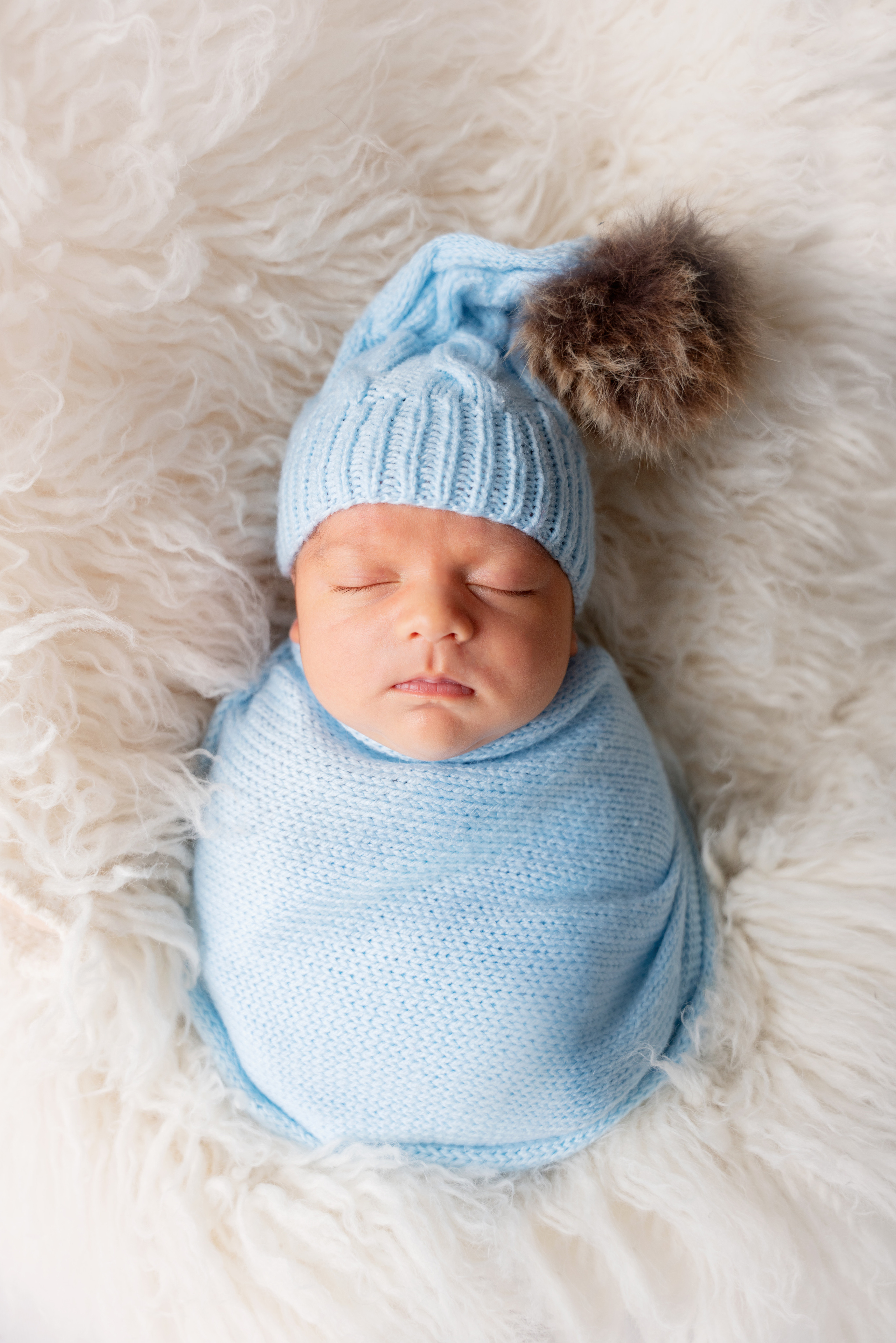 Baby in einem blauen Wickel und einem Hut mit Bommel