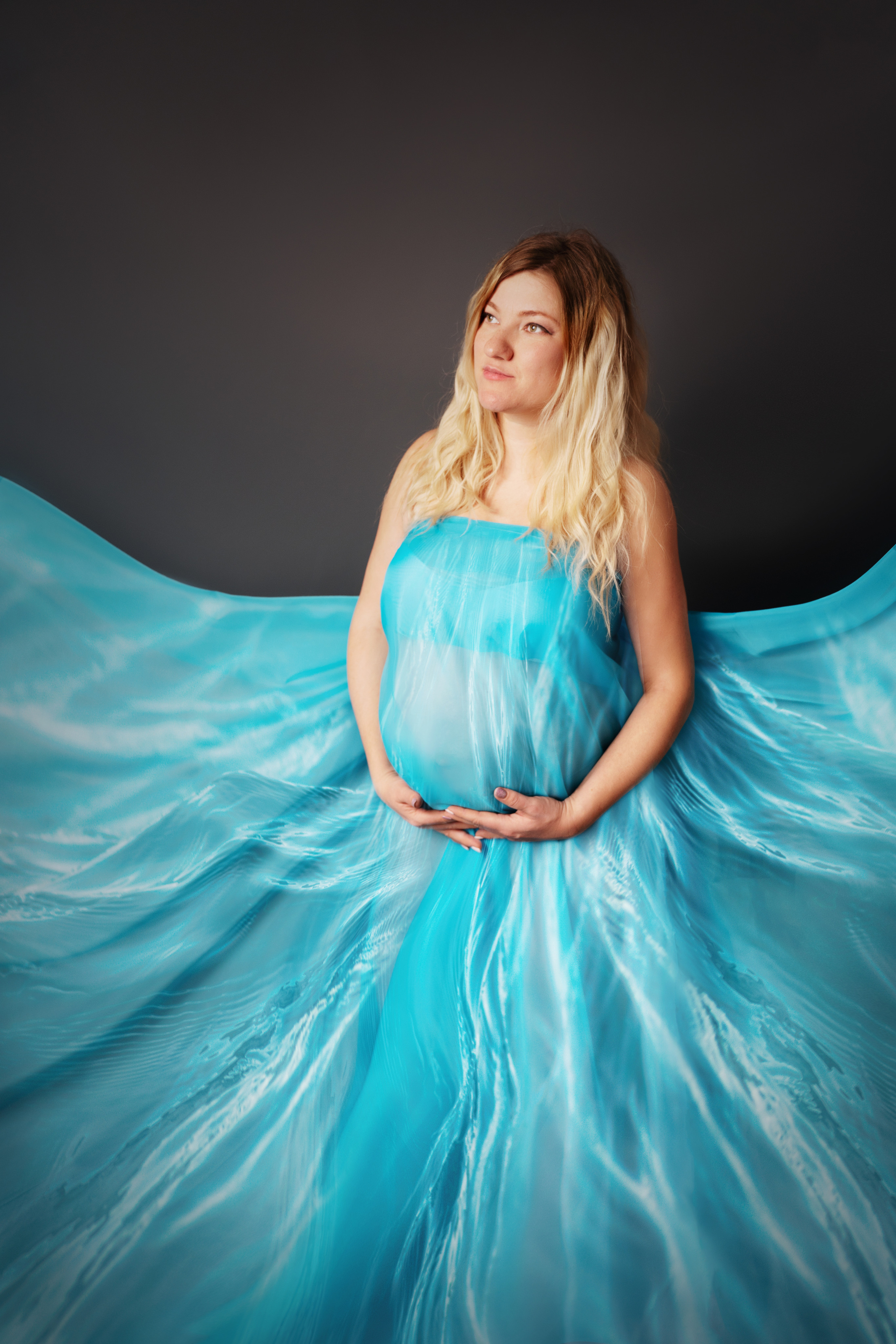 studio-shooting eines schwangeren mädchens in einem blauen fließenden kleid