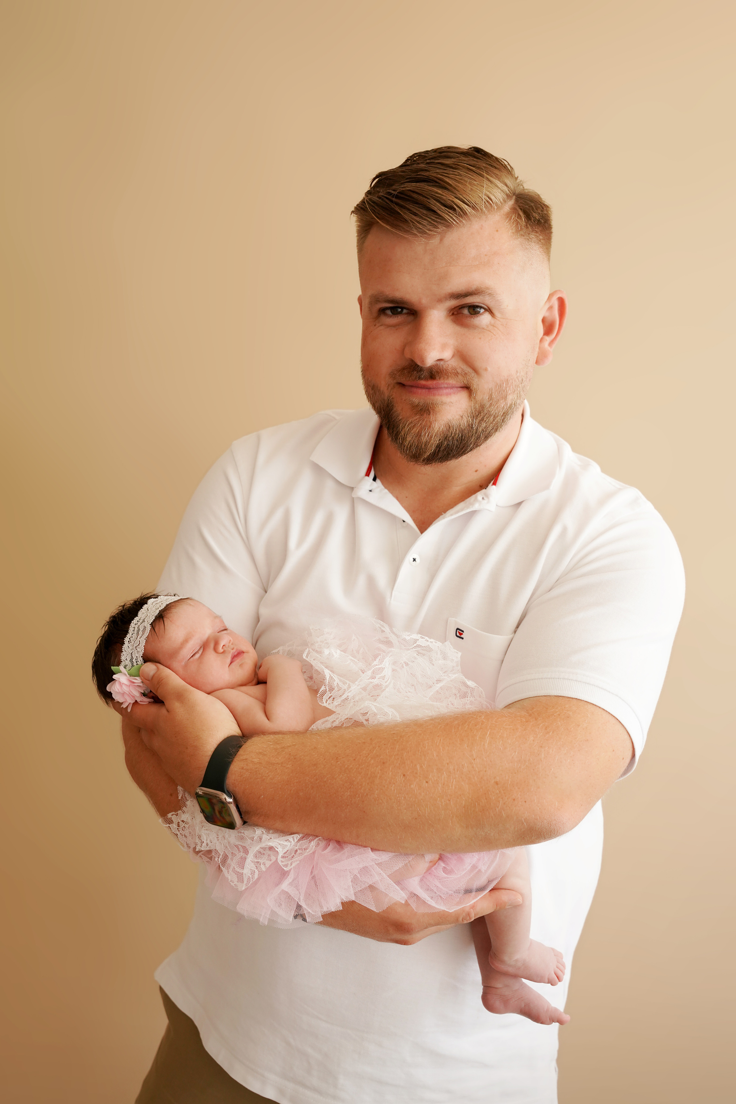 glücklicher Vater hält eine neugeborene Tochter mit einem Stirnband auf dem Kopf an den Händen