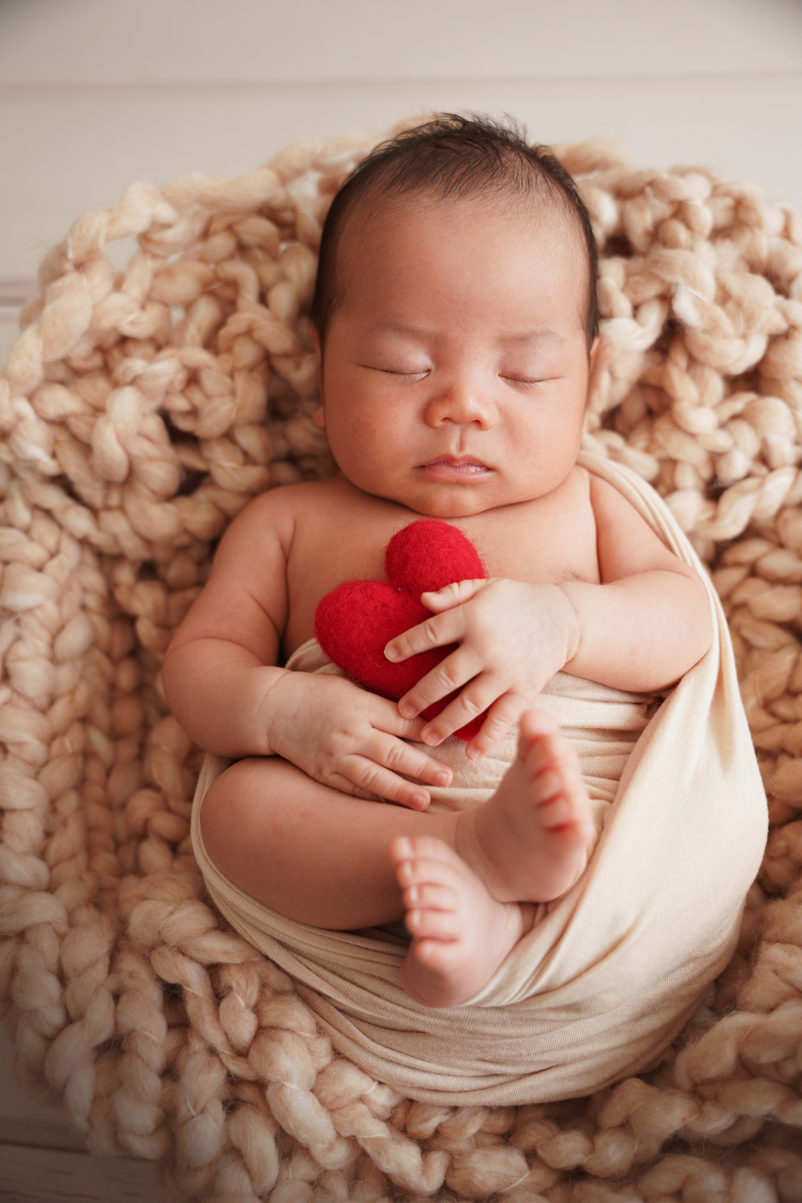 gewickelter Junge, der mit einem Wollherz in seinen Händen schläft