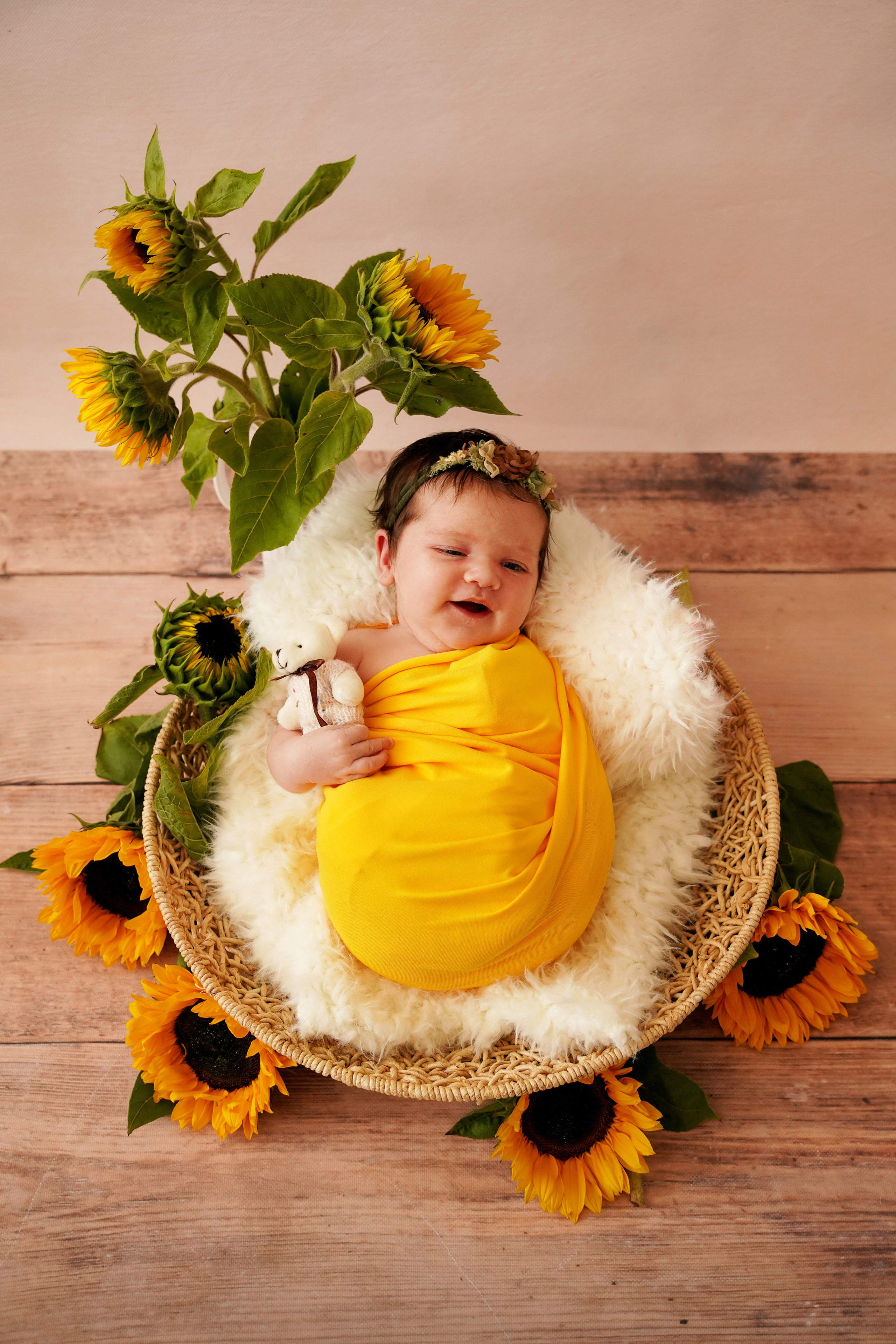 auf dem Bild liegen Sonnenblumen und ein kleines Mädchen in einer gelben Windel in einer runden Schüssel