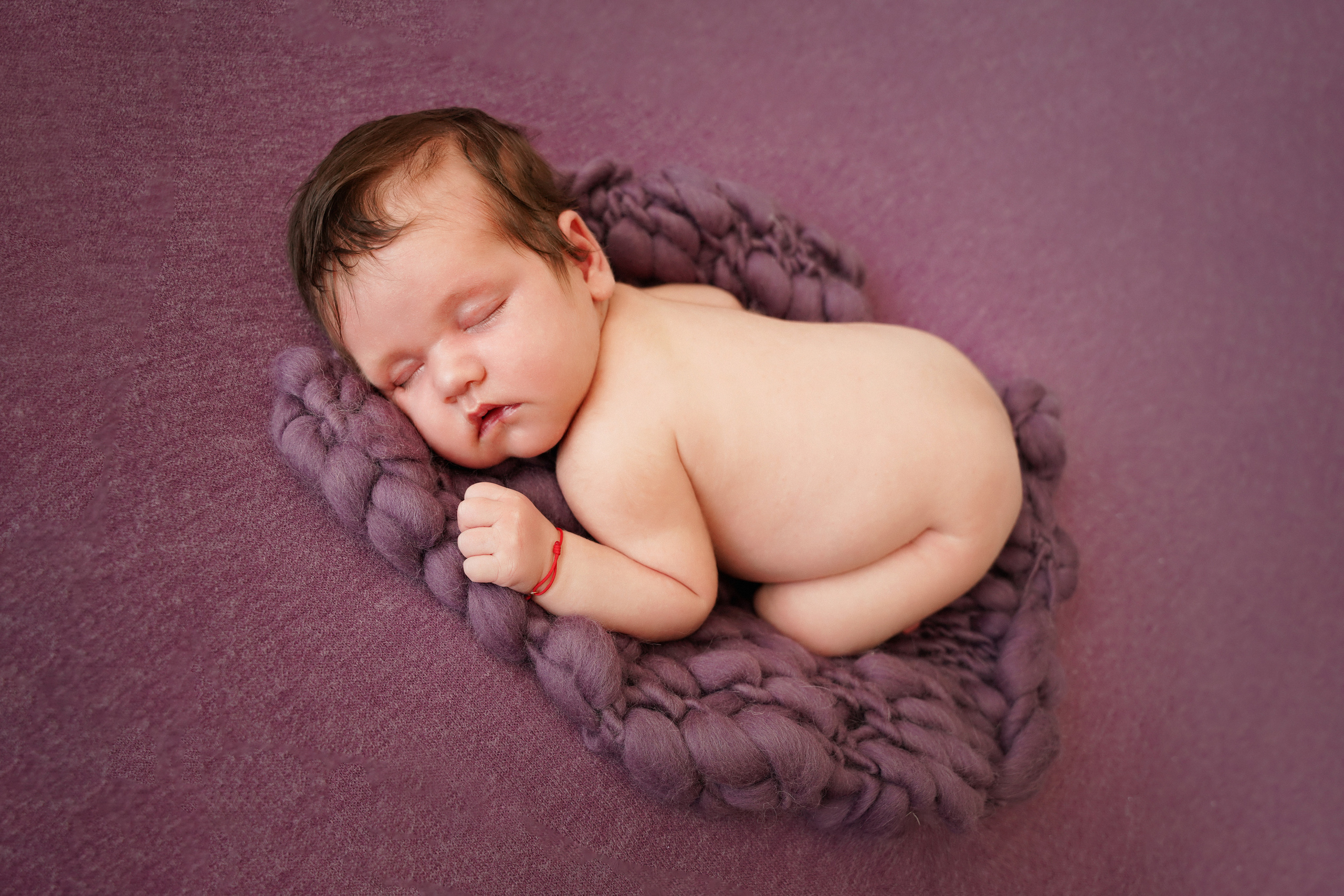 nacktes Baby liegt in einer Pose auf dem Bauch auf einer violetten Wolldecke