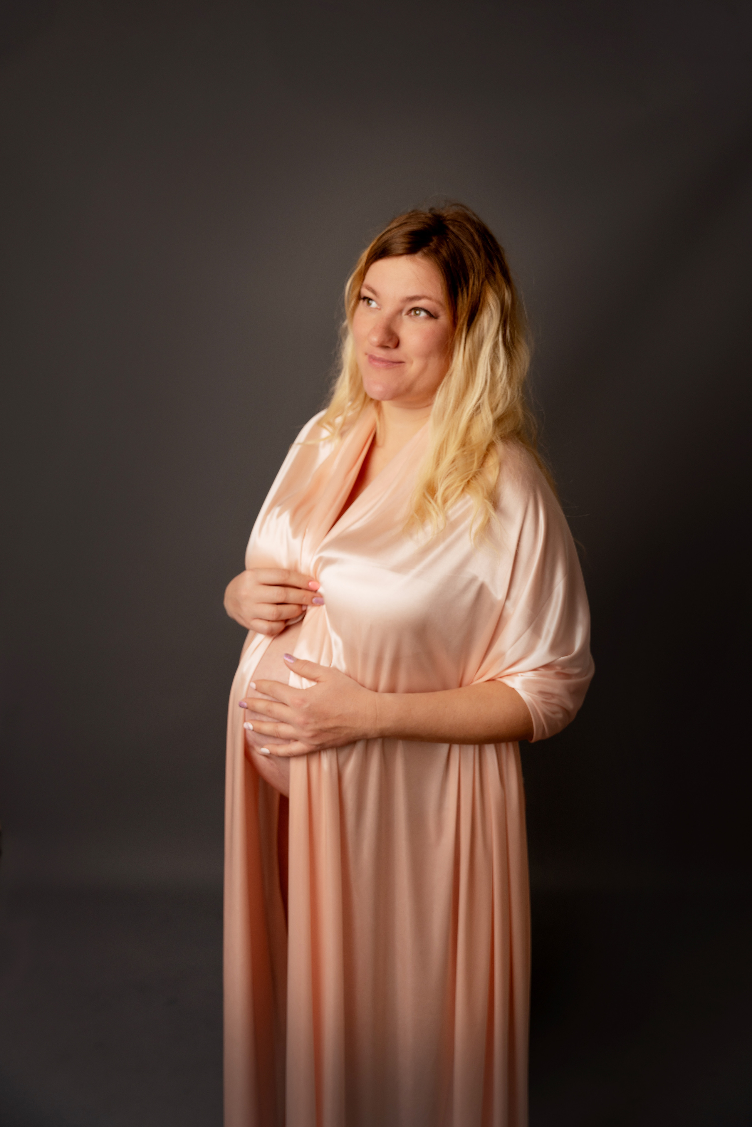 Auf dem Foto Schwangerin im Pfirsichkleid auf grauem Hintergrund