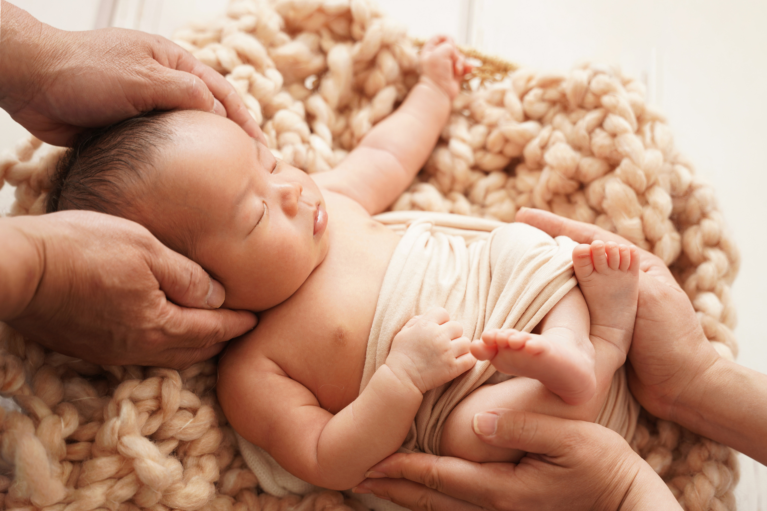 Das Baby liegt im Korb und sein Kopf und seine Füße werden von den Eltern aufbewahrt